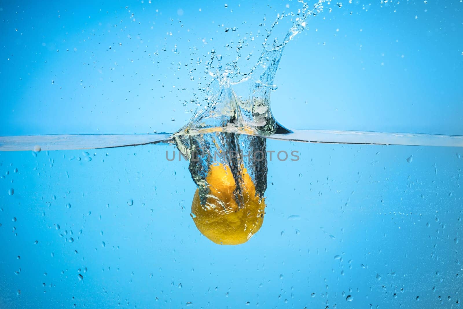 Single yellow lemon being dropped in blue water