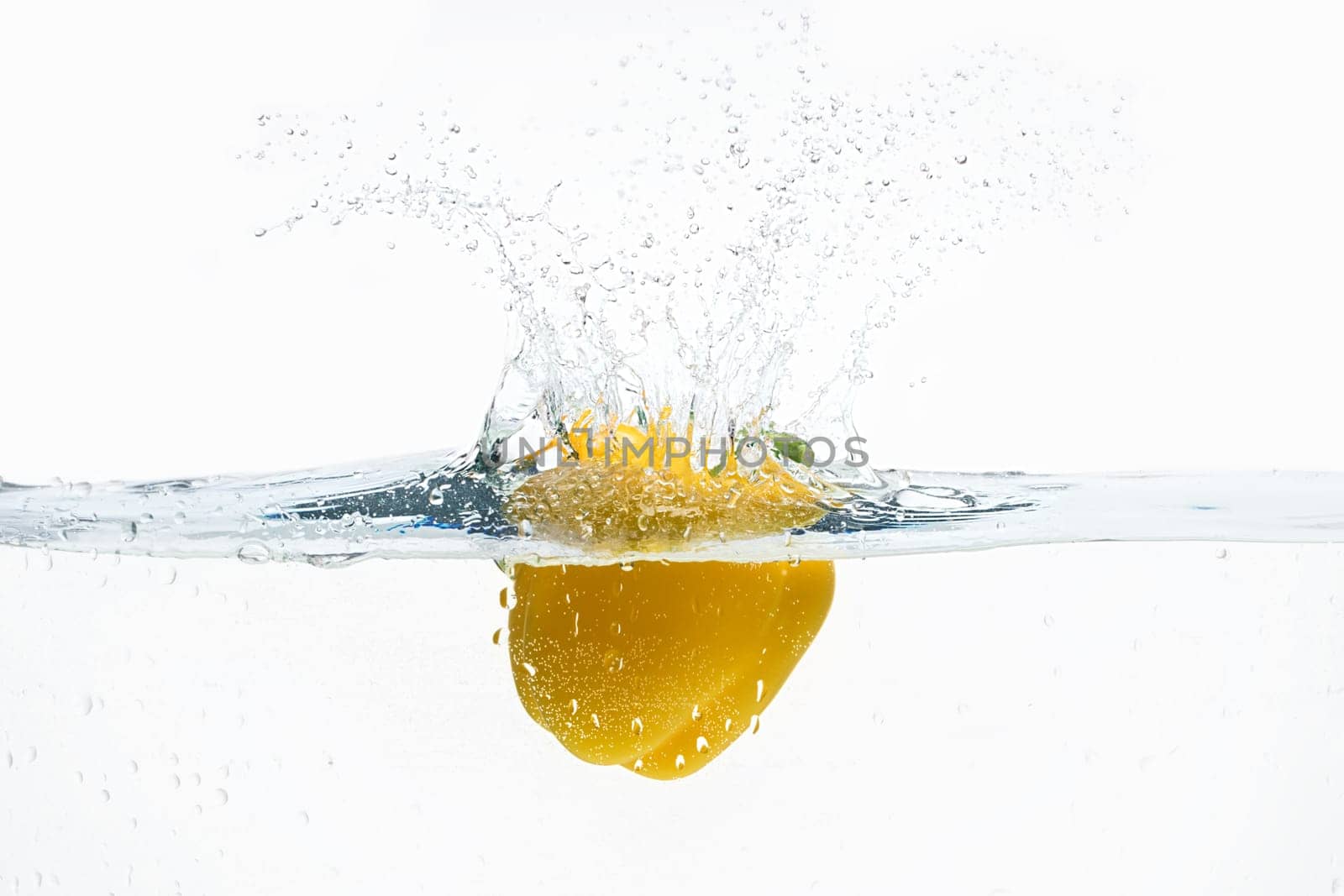Sweet yelllow pepper thrown in water from top with splashes above it