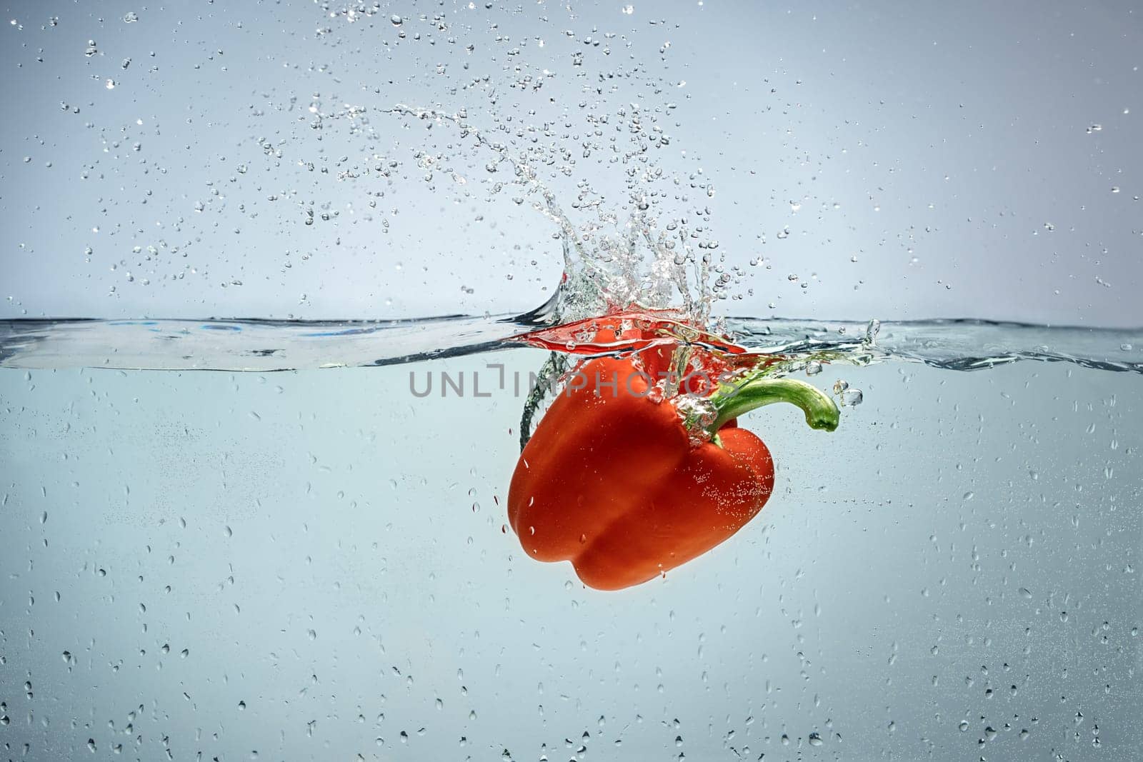 Single red pepper being dropped in blue water