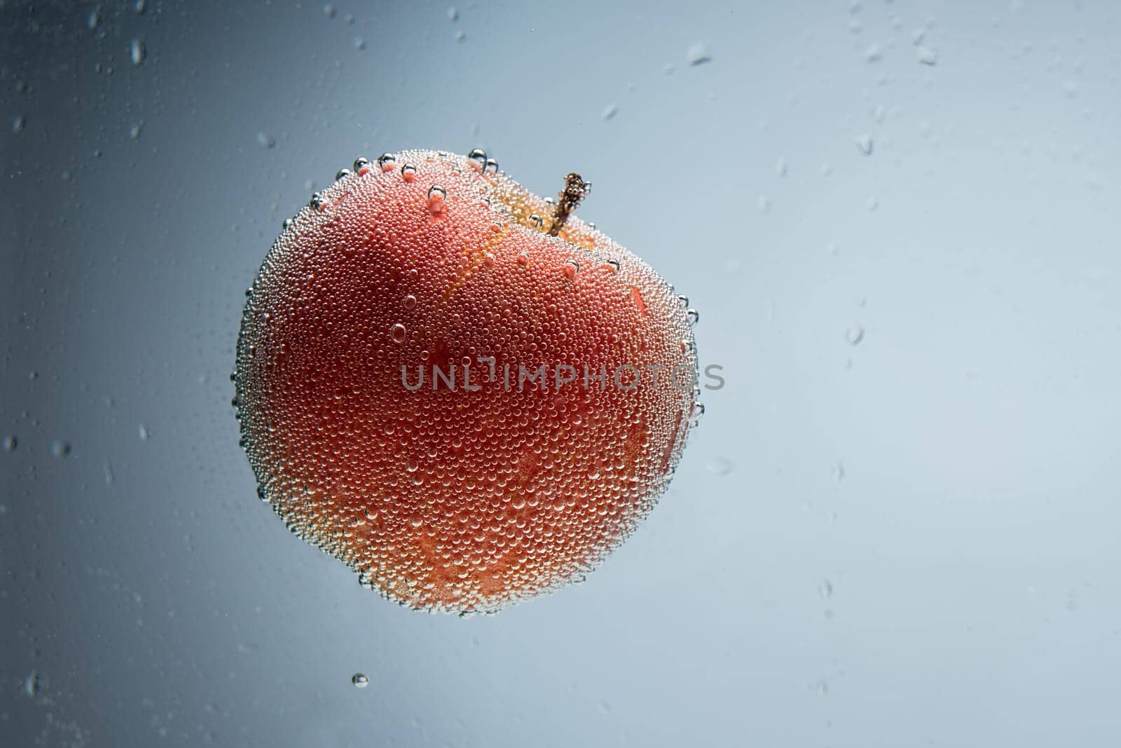 Single red apple covered with air bubbles floating in blue water