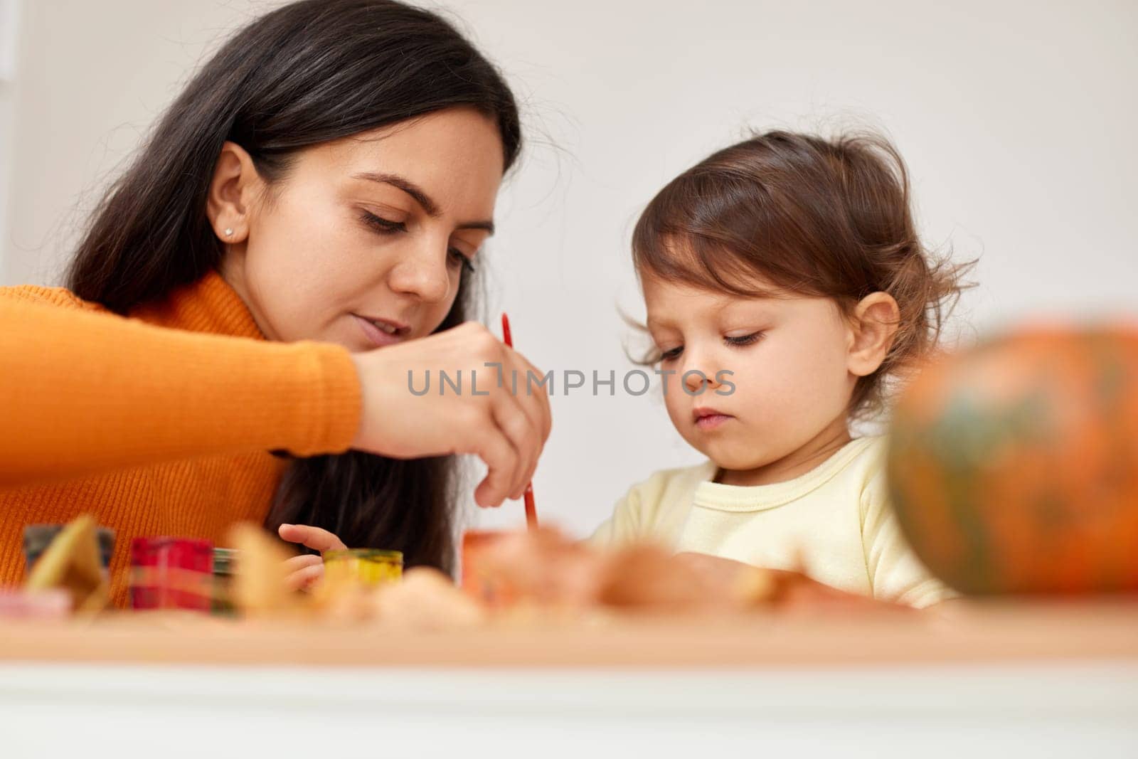 happy little child girl and her mother drawing for the autumn holiday. Happy family making autumn decorations together