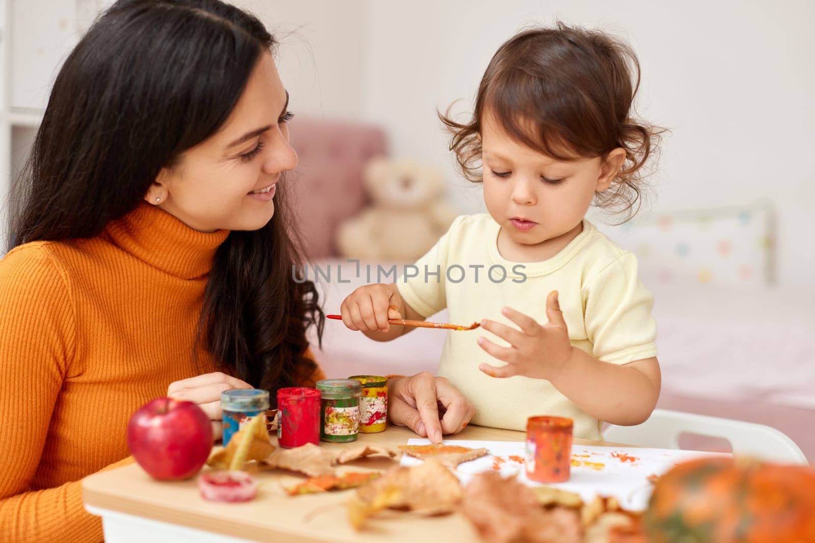 Cute little girl and mom spending good time painting autumn yellow leaves together