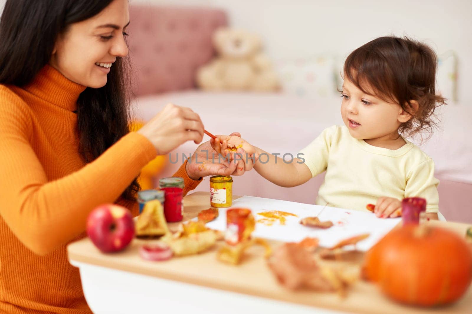 Cute little girl and mom spending good time painting hands and autumn yellow leaves together