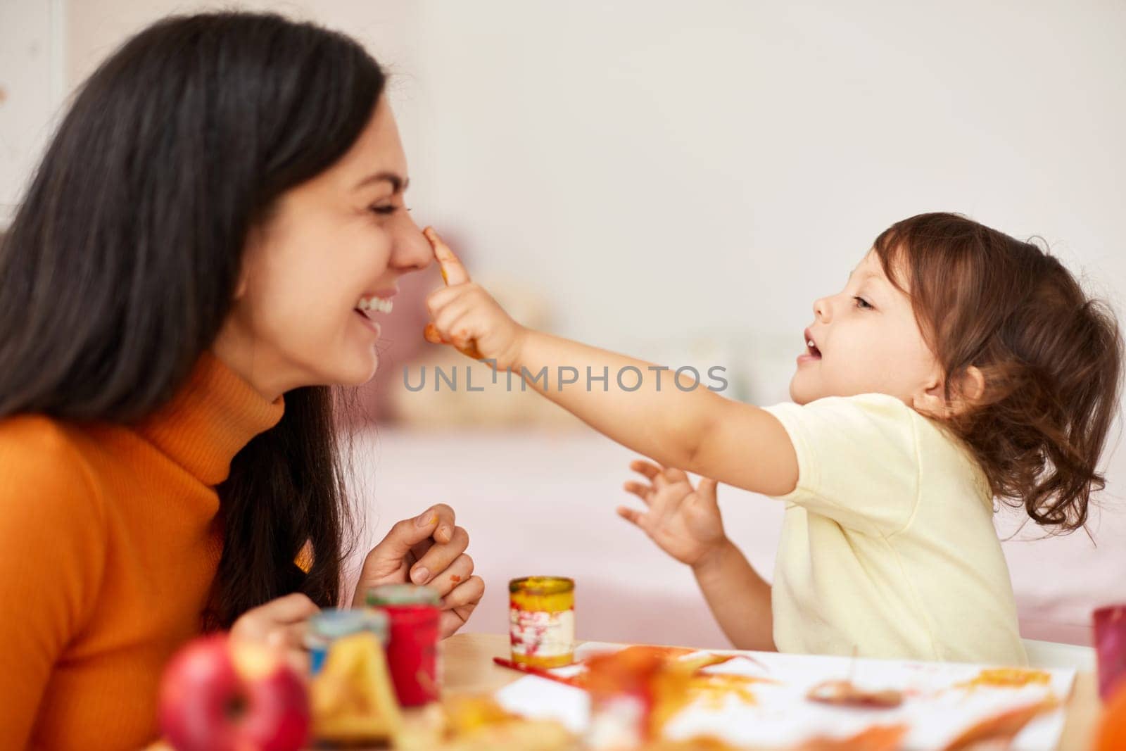 Cute little girl and mom spending good time painting autumn yellow leaves together