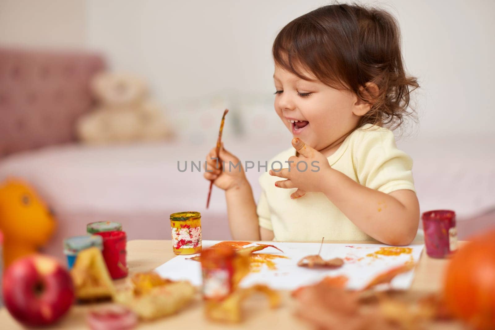 happy little child girl painting autumn leaves. smiling baby girl drawing leaves in yellow paint