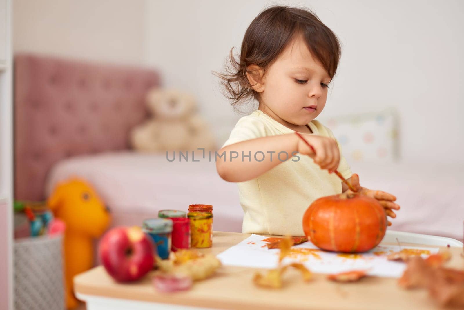 happy little child girl painting Halloween pumpkin. smiling baby girl drawing autumn pumpkin in yellow paint