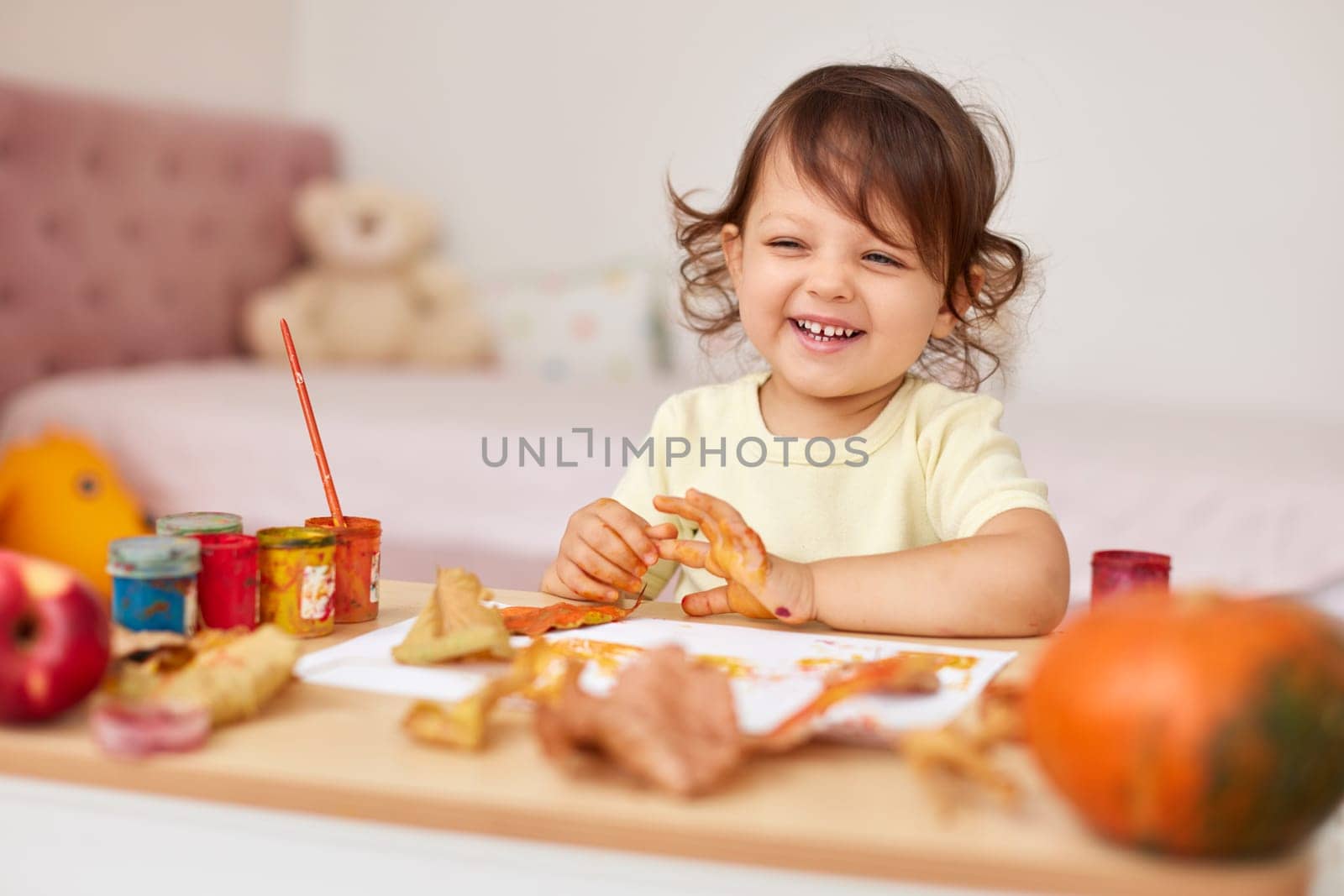 happy little child girl painting autumn leaves. baby girl drawing leaves in yellow and orange paint