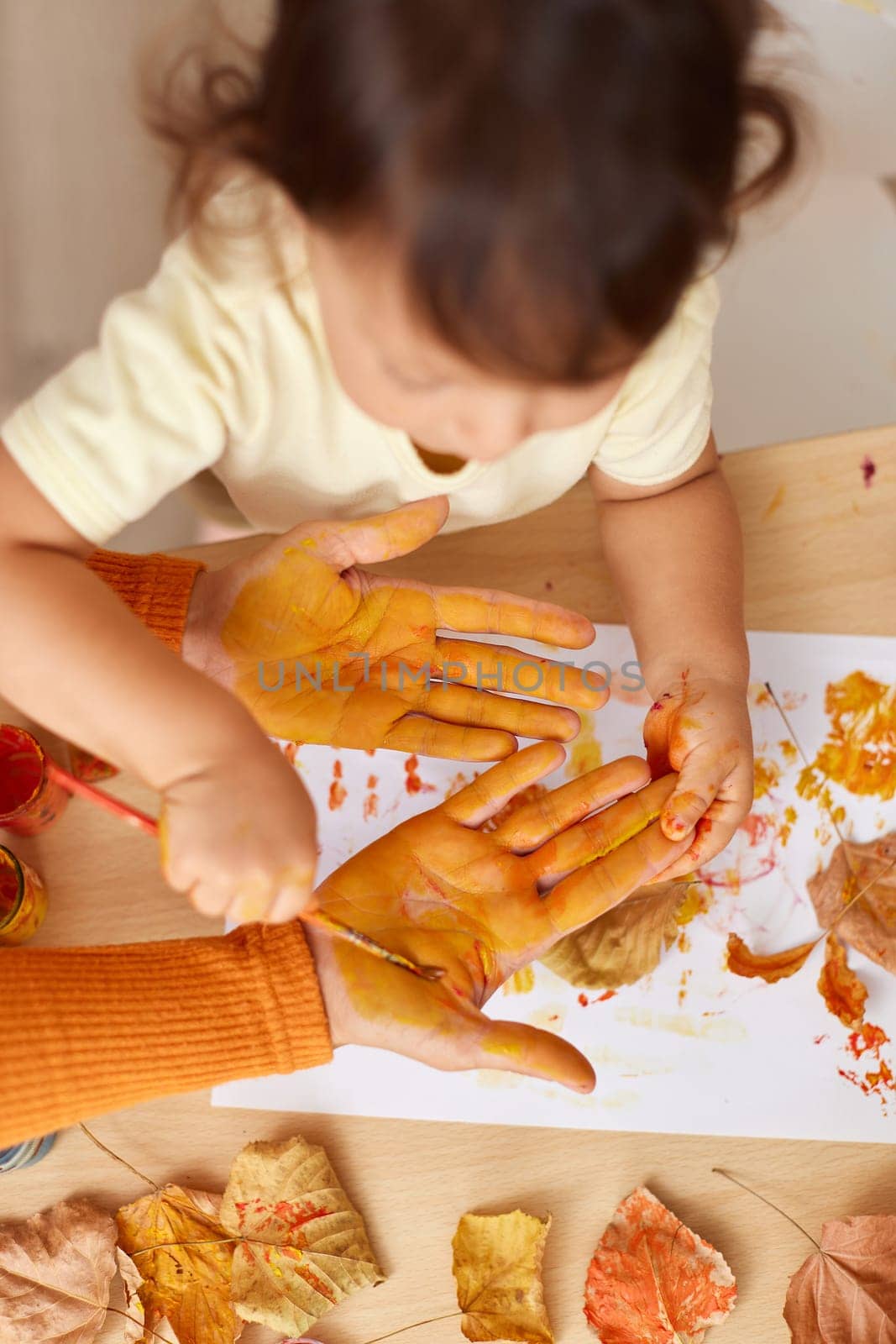 little child girl and mother painting hands and autumn leaves together. mom and baby showing hands in yellow paint. top view