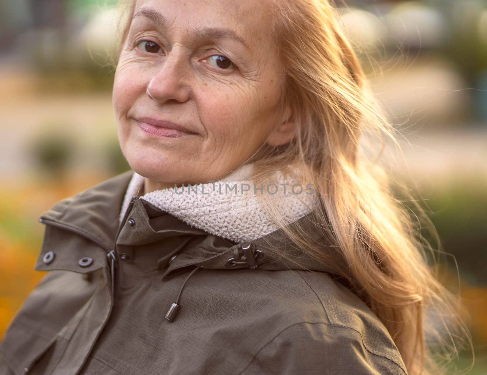 An elderly 60 beautiful woman with a kind smile is walking outdoors on a sunny autumn day, a happy old lady, a grandmother takes care of her appearance, natural beauty with wrinkles portrait closeup.