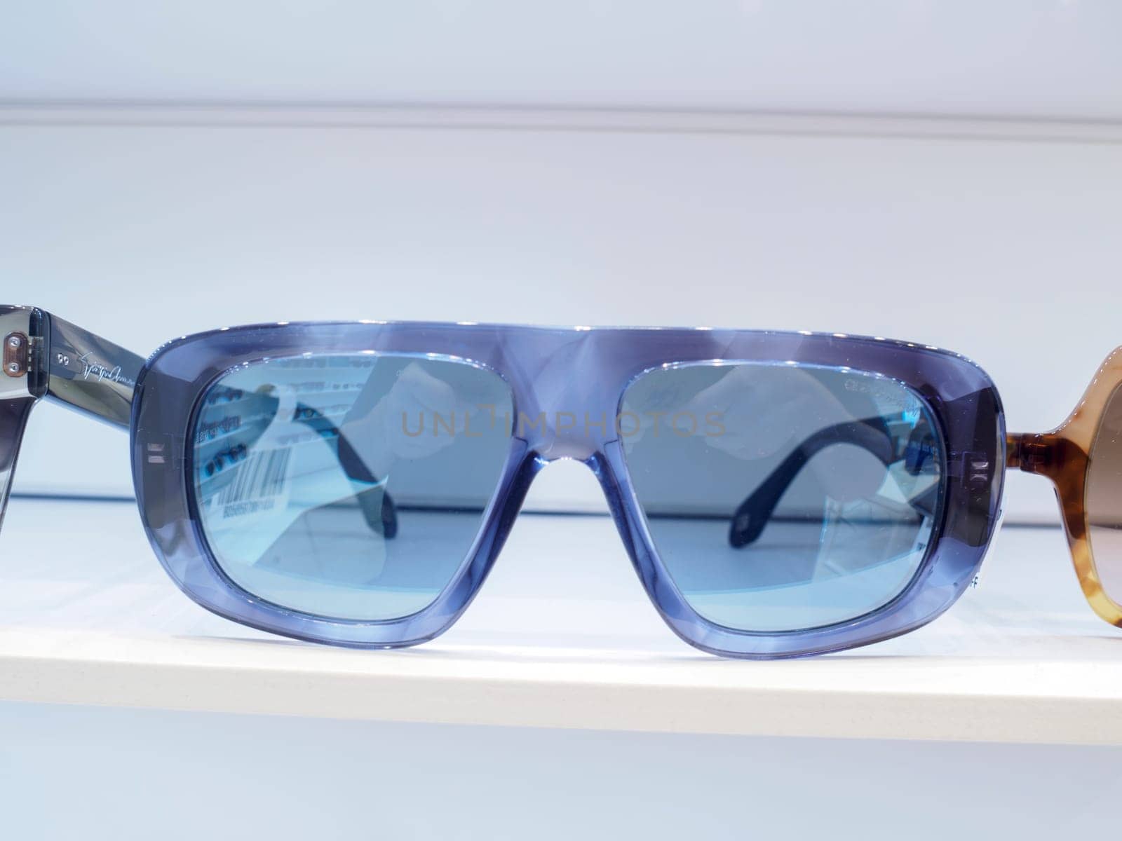 Blue fashion sunglasses with thick frames and blue lenses sit on a white shelf, reflecting the inside of an optometrist's office