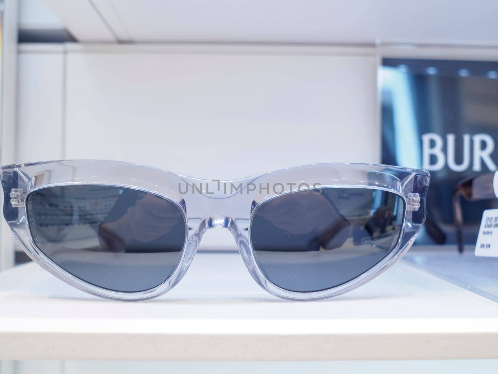 Pair of modern cat eye sunglasses are displayed on a shelf in an upscale retail store, reflecting the surrounding lights and interior