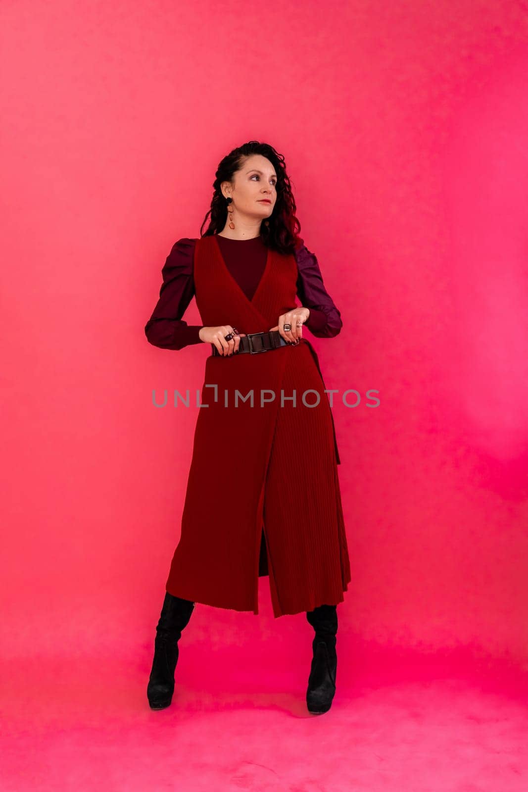 A woman in a red dress poses for the camera. She is wearing black boots and a belt