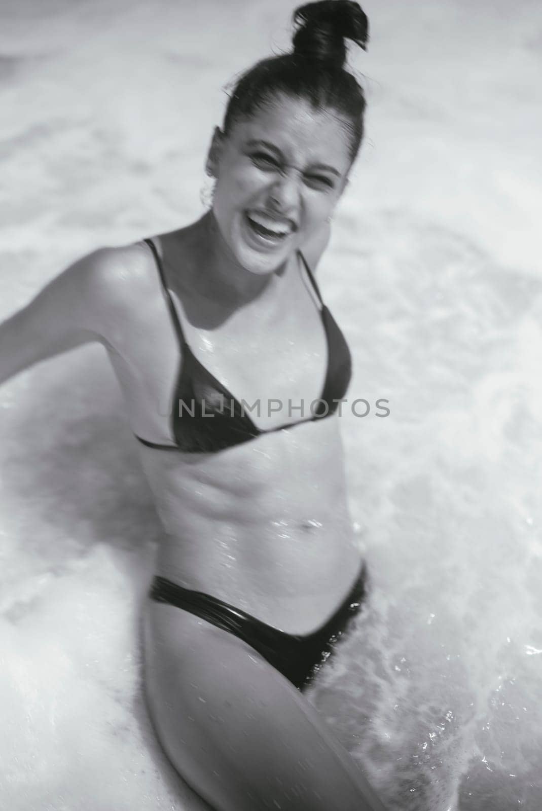 A young woman enjoys a beach day, radiating happiness in a stylish bikini surrounded by ocean waves
