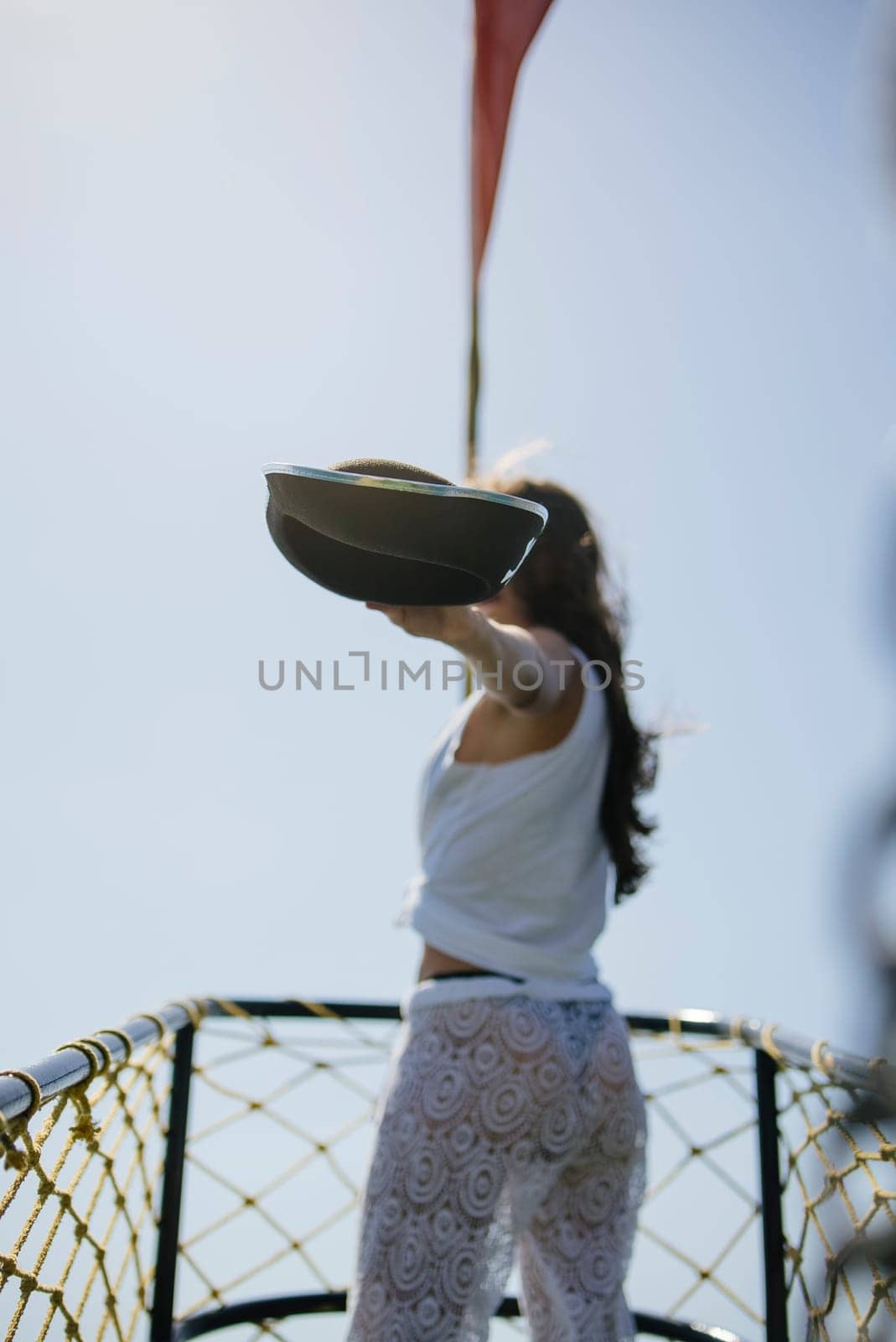 A confident woman stands on a ship while holding a stylish hat, fully enjoying the bright and sunny atmosphere