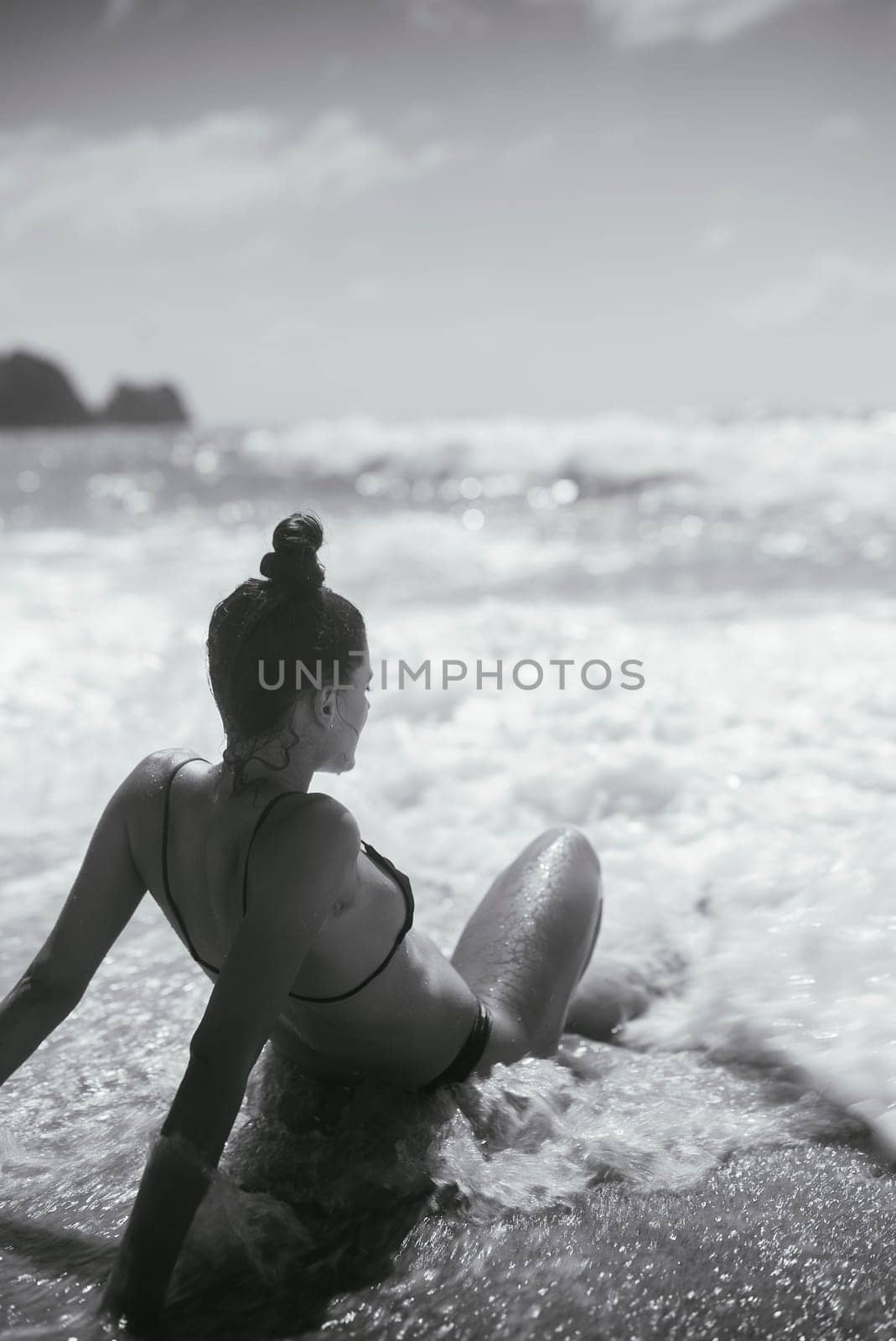 A stunning black and white image of a woman seated by the waves, embodying peace and nature's beauty.