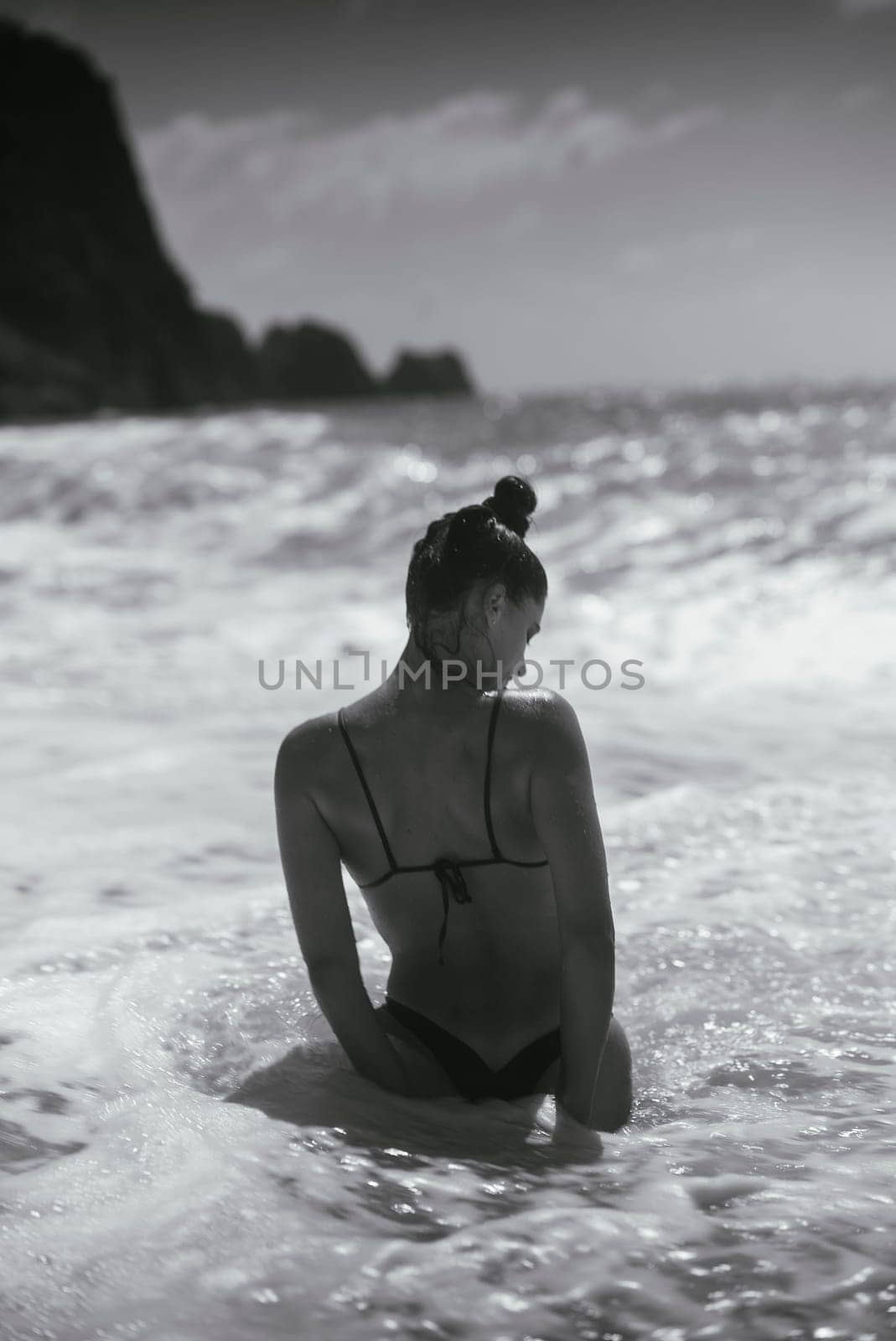 A woman in a stylish bikini enjoys ocean waves, captured in classic black and white, evoking elegance and tranquility