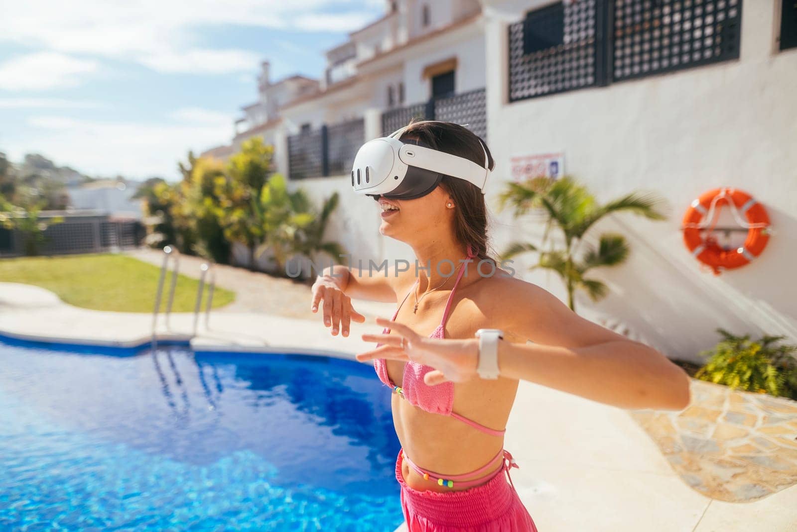 A woman wearing VR goggles fully engages with an exciting immersive virtual experience by a bright, sunny poolside