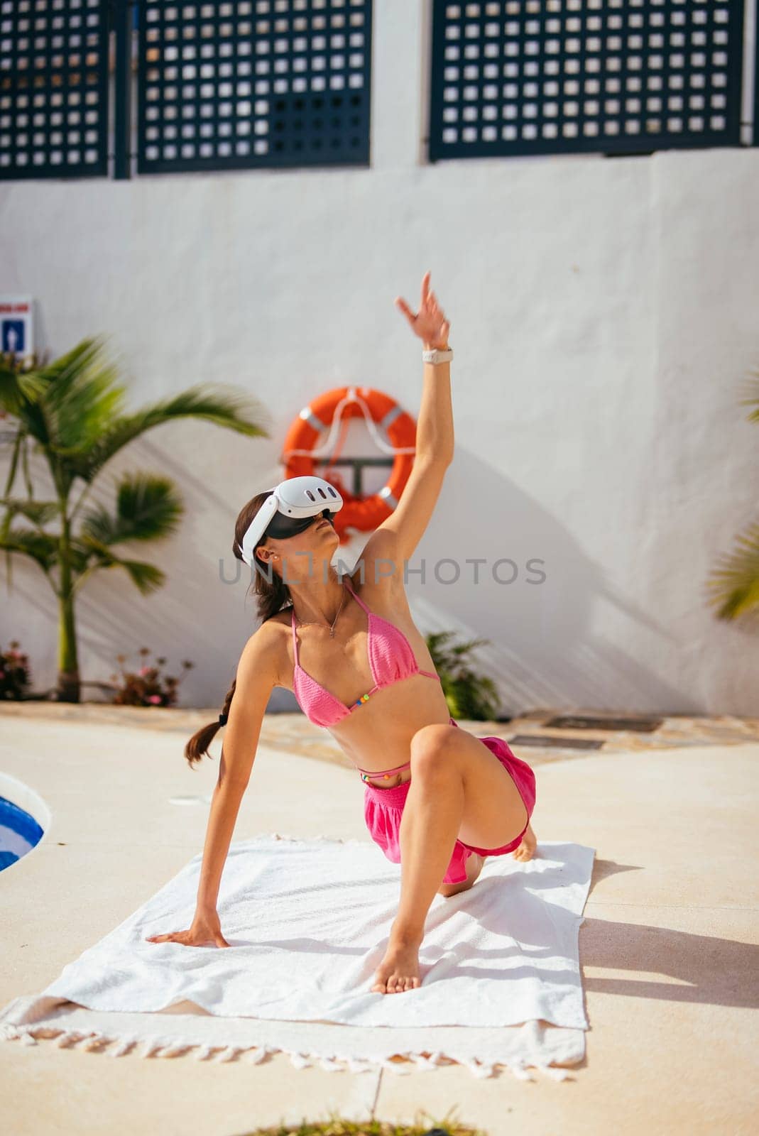 A joyful and playful woman wearing a pink bikini poses beside the pool on a beautiful sunny day, radiating happiness