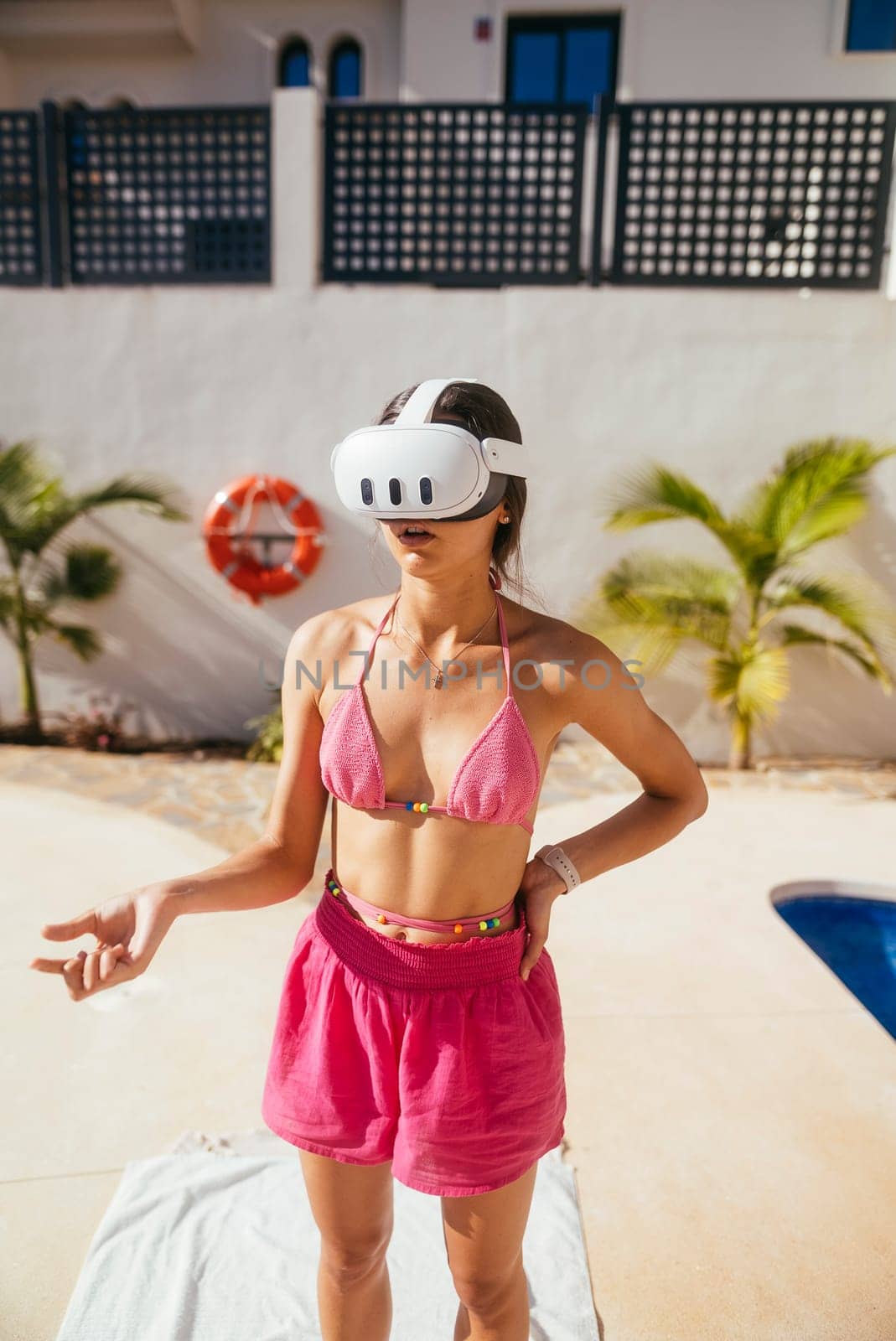 A young woman happily enjoys a VR experience while relaxing poolside this summer in colorful attire