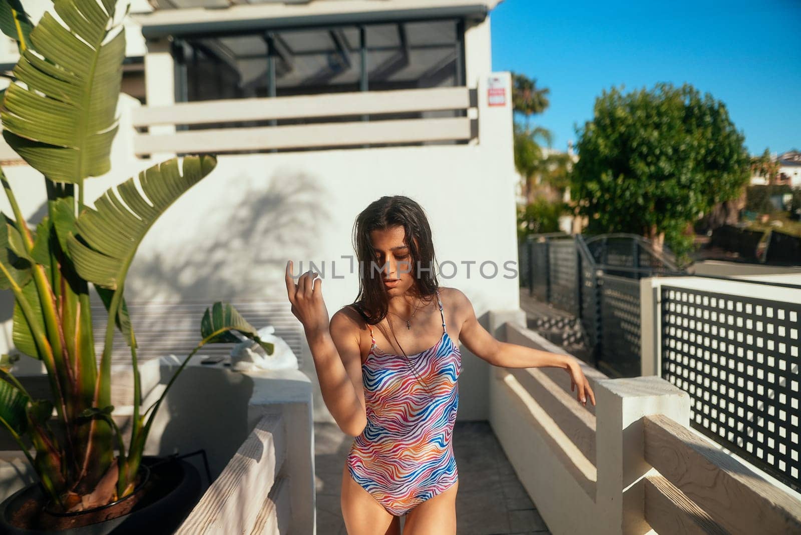 A young and vibrant woman poses in a colorful swimsuit near a sparkling pool, fully embodying the joyful summer vibes