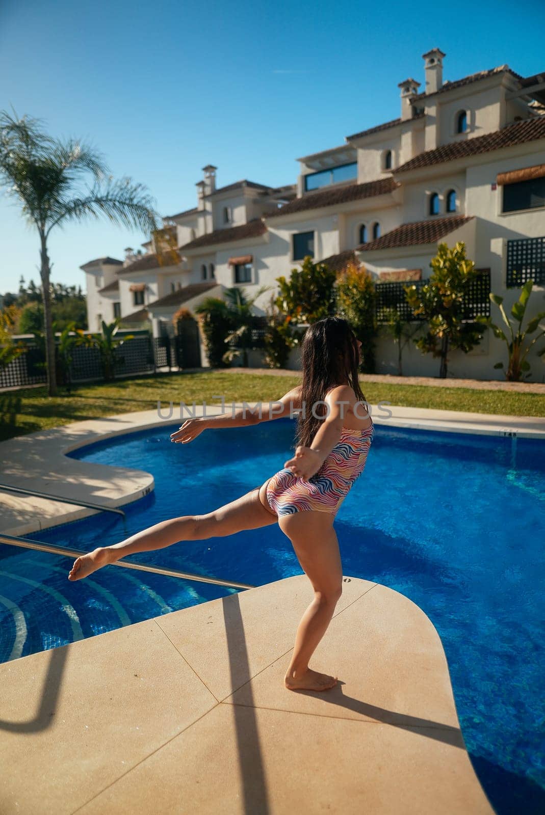 A young girl is happily dancing joyfully by the shimmering, picturesque pool on a bright sunny summer day