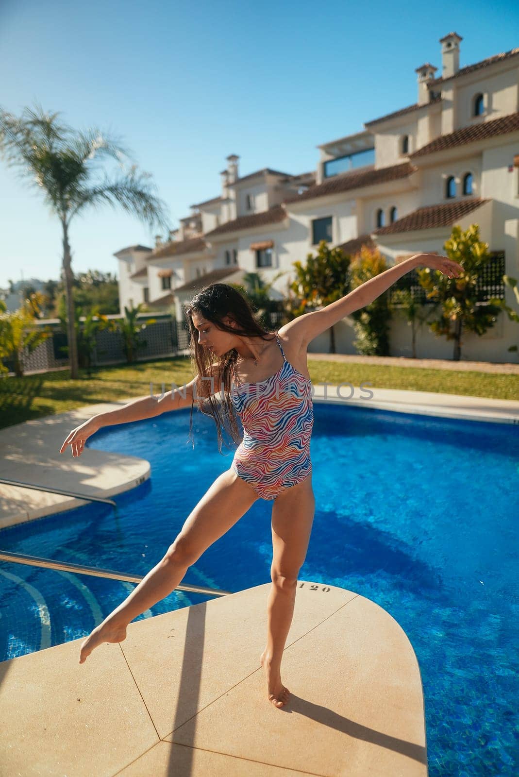 A talented and young dancer is showcasing her incredible agility and skill by balancing elegantly at a poolside