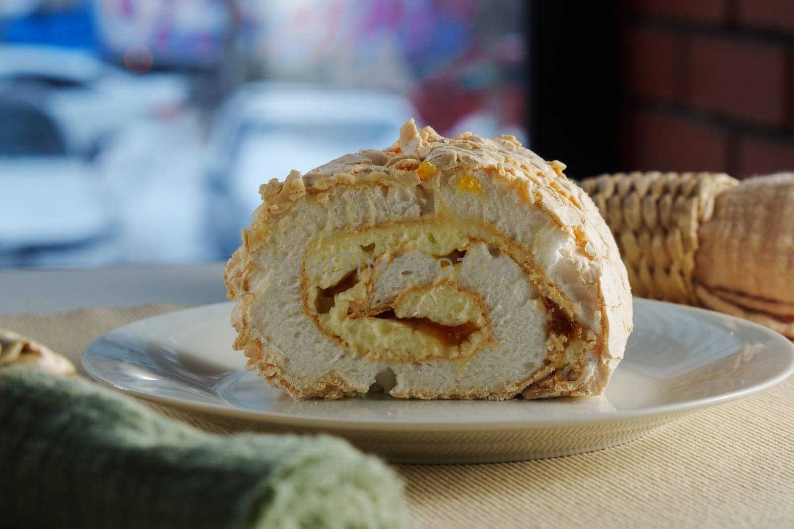 A beautifully crafted dessert roll sits elegantly on a plate, revealing layers of cream and sweet filling, complemented by a lively urban backdrop.