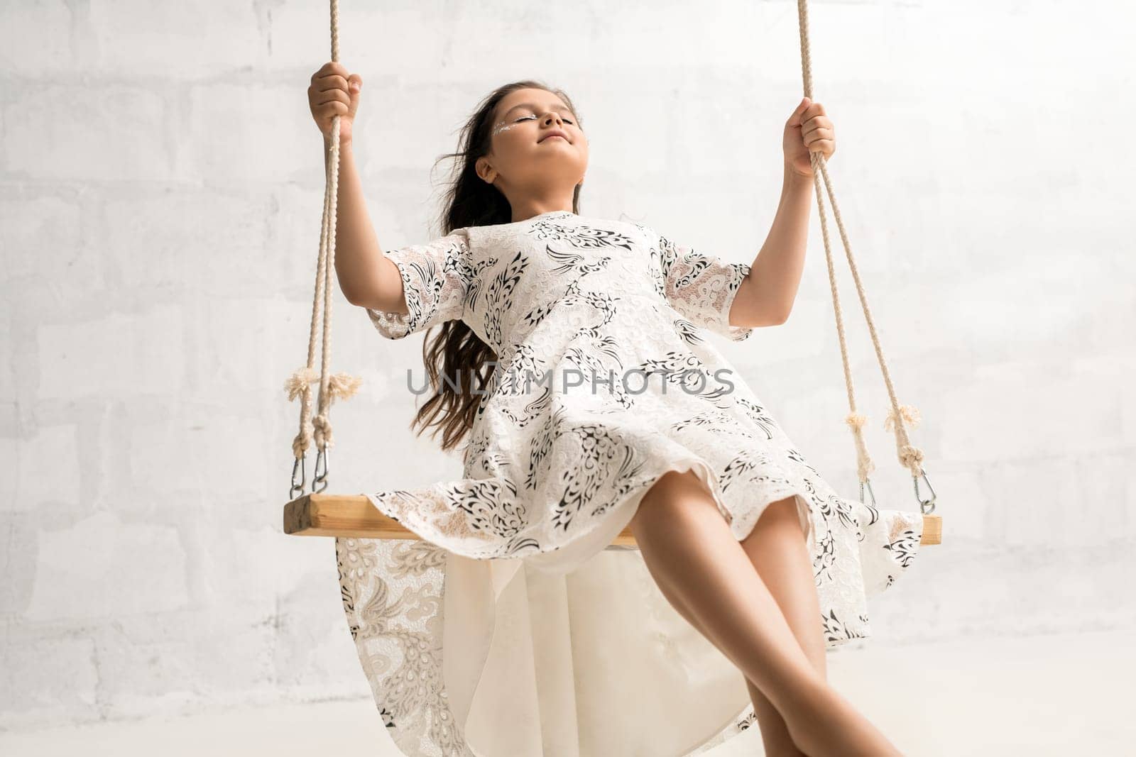 Tennaged pretty girl with fantasy makeup and curly long hair wearing nice dress swinging with her eyes shut romantic sunny shot