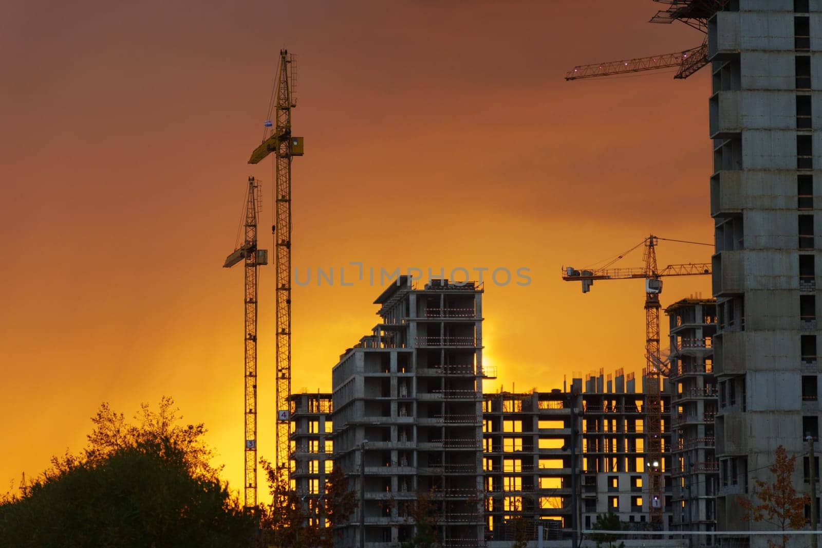 Golden sunset behind a bustling construction site with cranes and buildings silhouetted against the vibrant sky