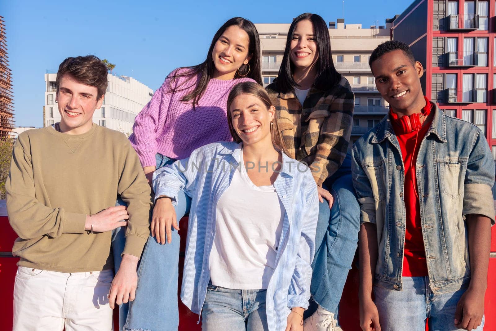 Multiracial group of students looking at the camera laughing outdoors at the university. Young community of people having fun together.