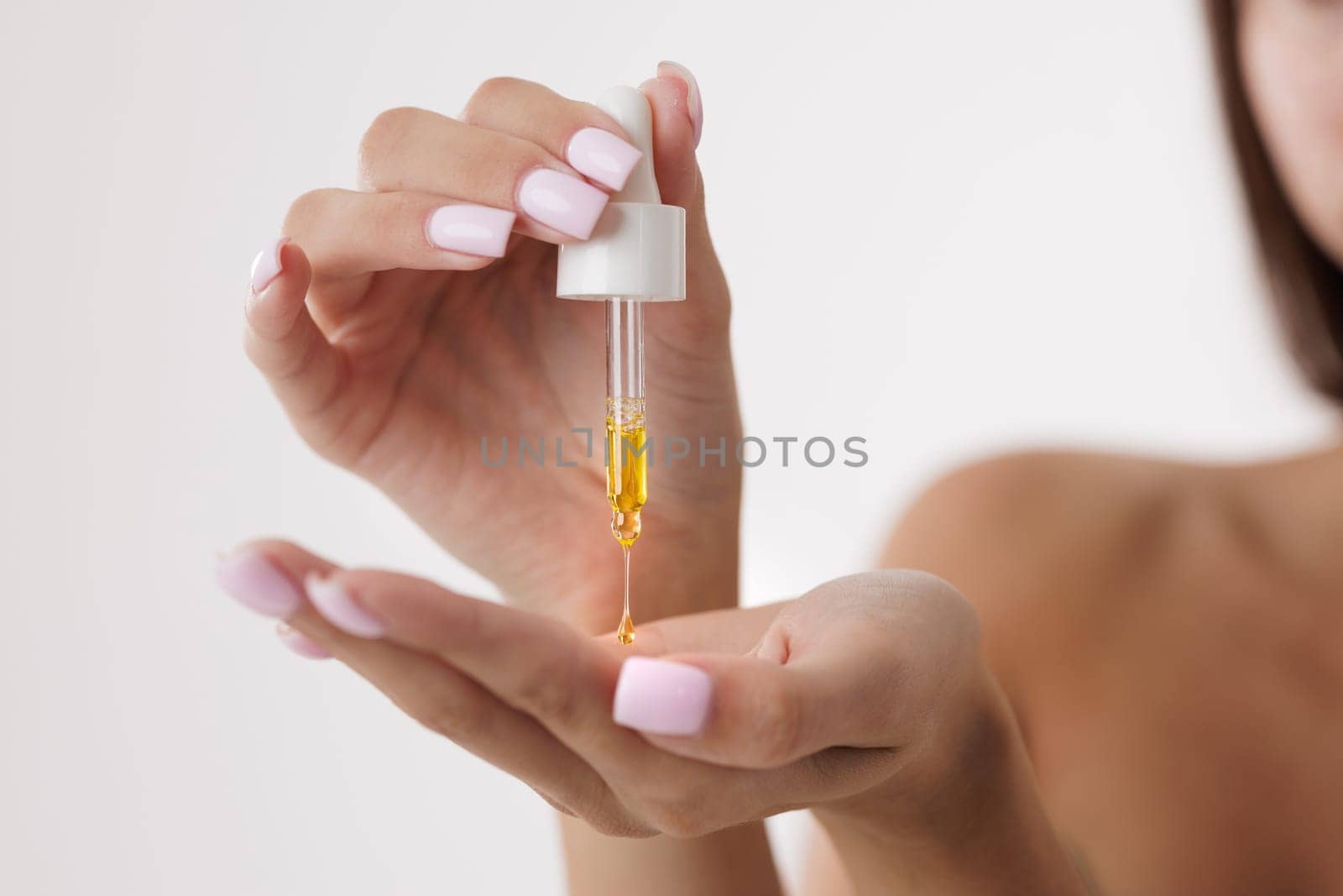 Close up of woman applying organic face and body oil with pipette, dripping a drop of oil onto her palm,
