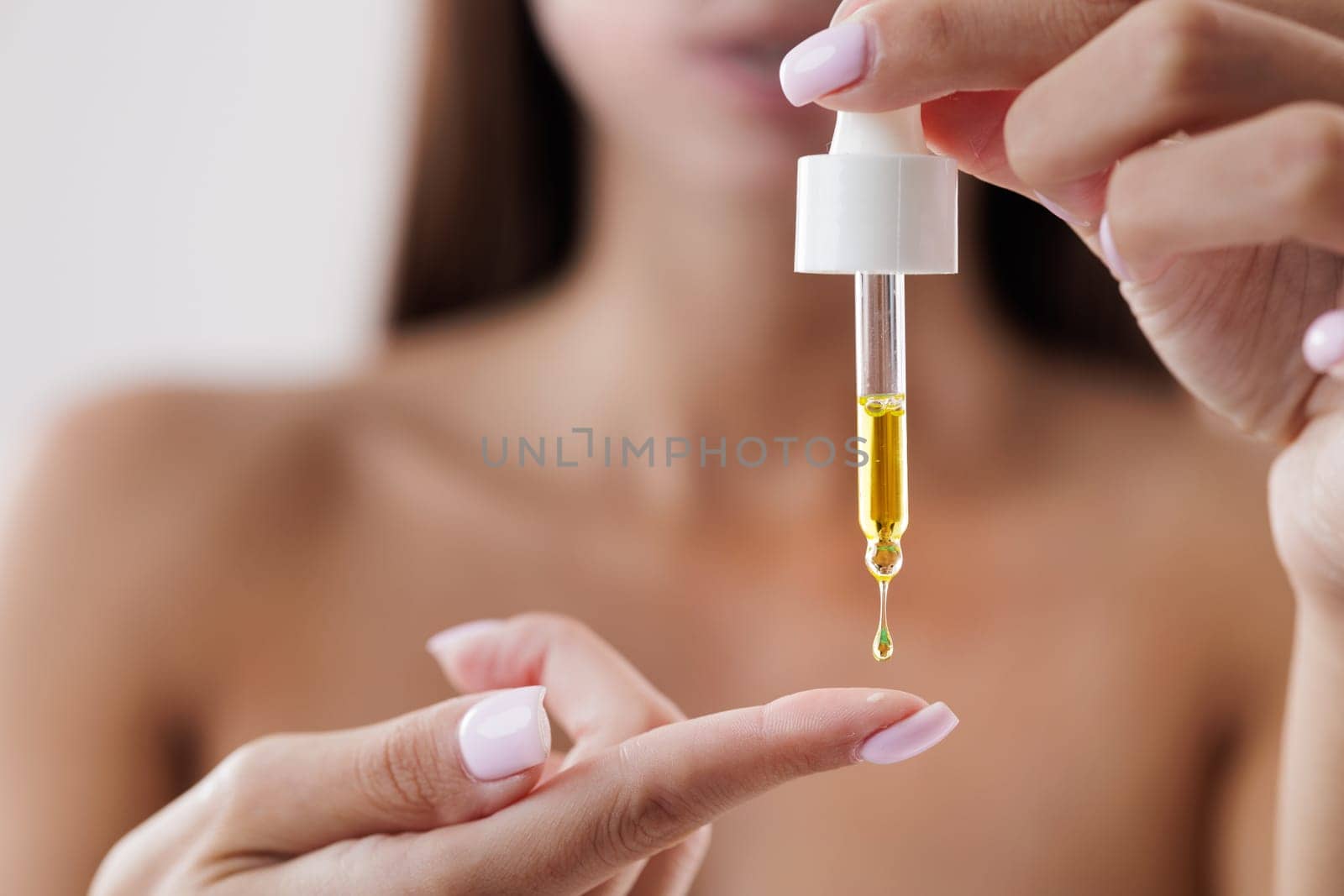 Beautiful girl dripping skin care product on her finger with a pipette, close-up, vitamins or natural oils on a white isolated background