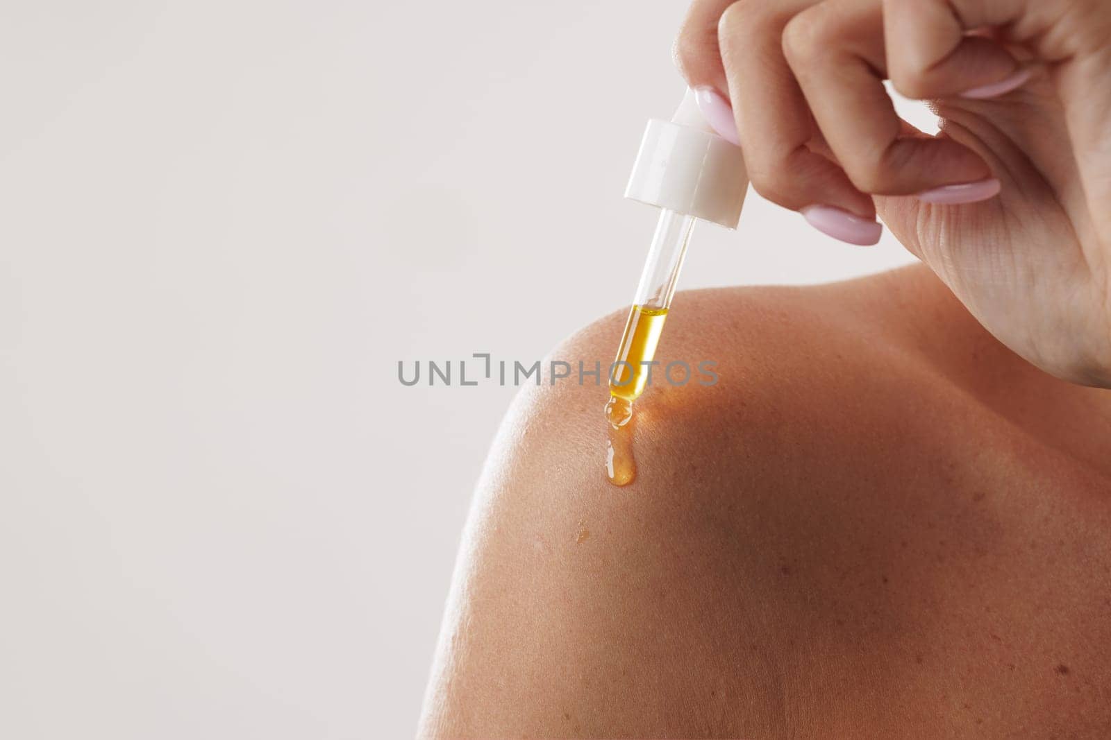 woman applying oil and serum on body with pipette close-up, on white background, concept of body and skin care