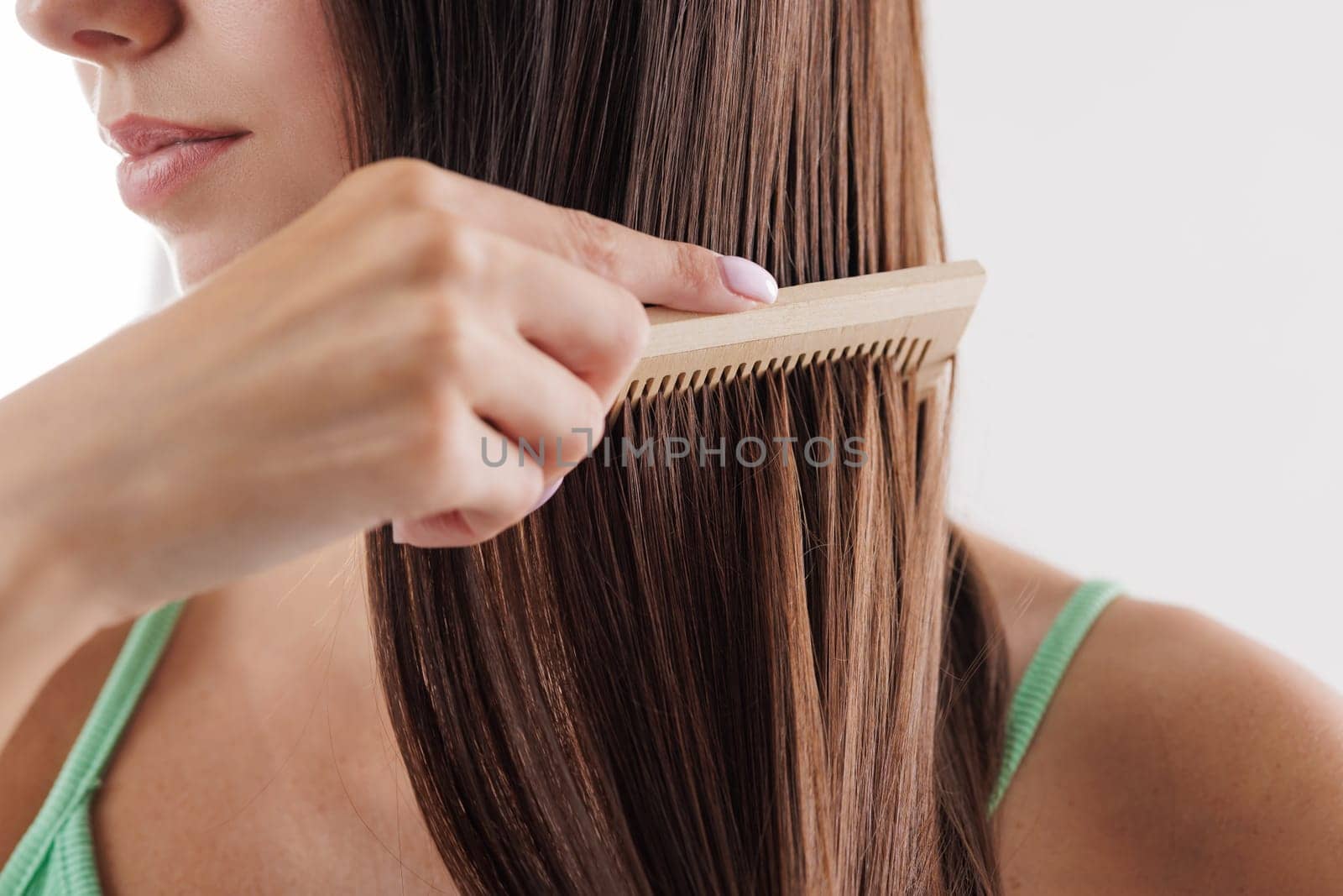 Close up of woman combing her long straight brown hair with wooden comb. hair care, hair problem