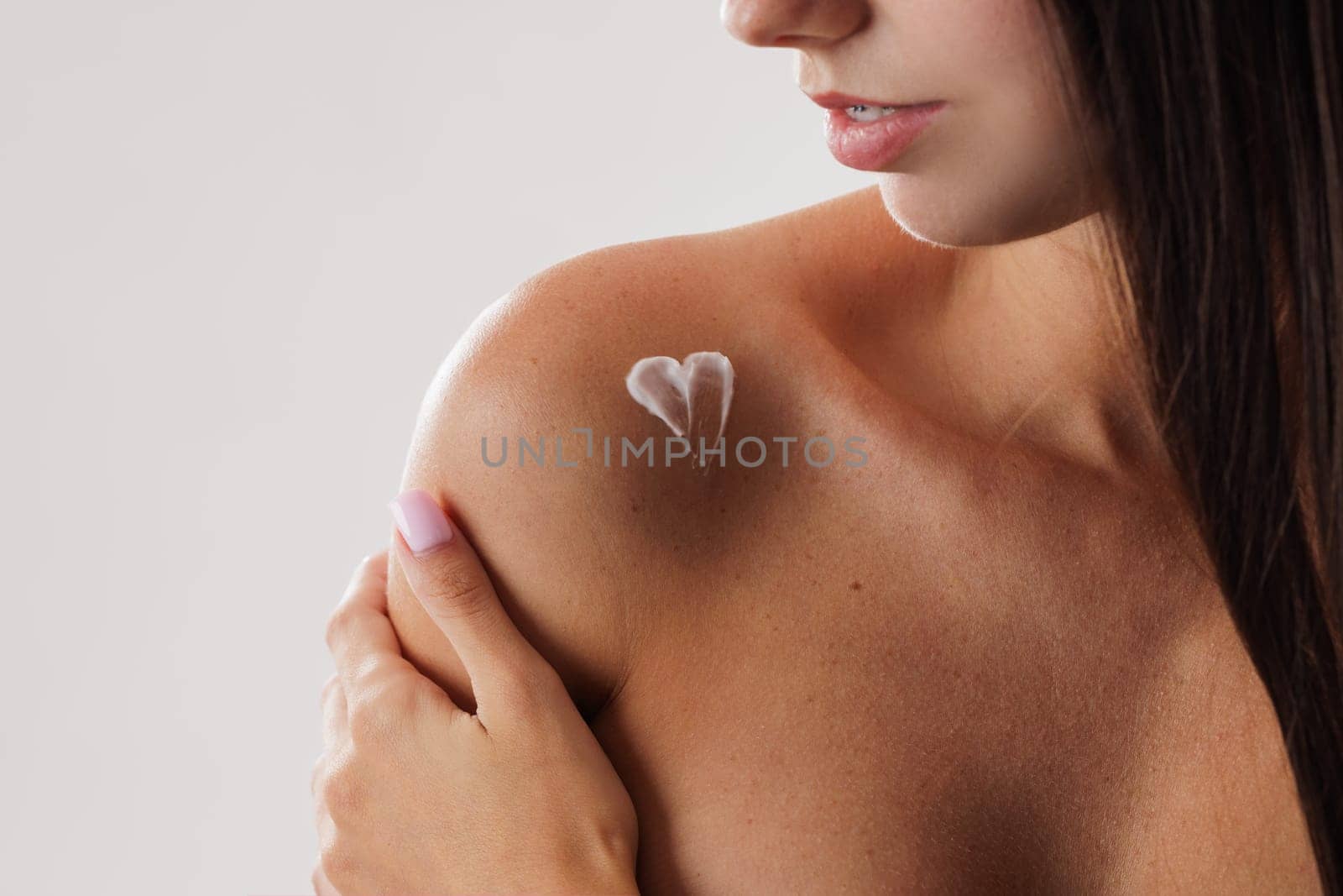 Close up of woman's shoulder with heart shaped cream or lotion applied on skin, body care concept