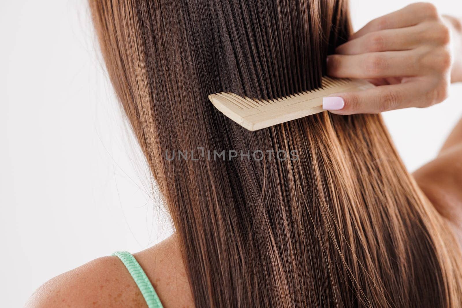 A person combing their long, straight brown hair with a wooden comb. hair care, hair problem
