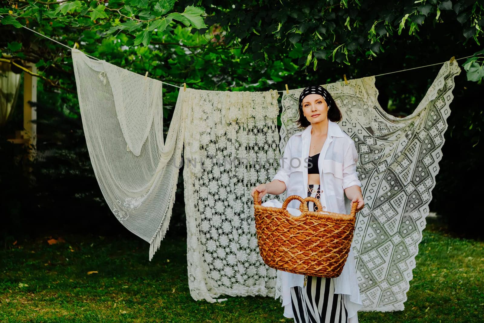 Woman stands in a lush green garden, hanging intricate lace fabric on a clothesline.
