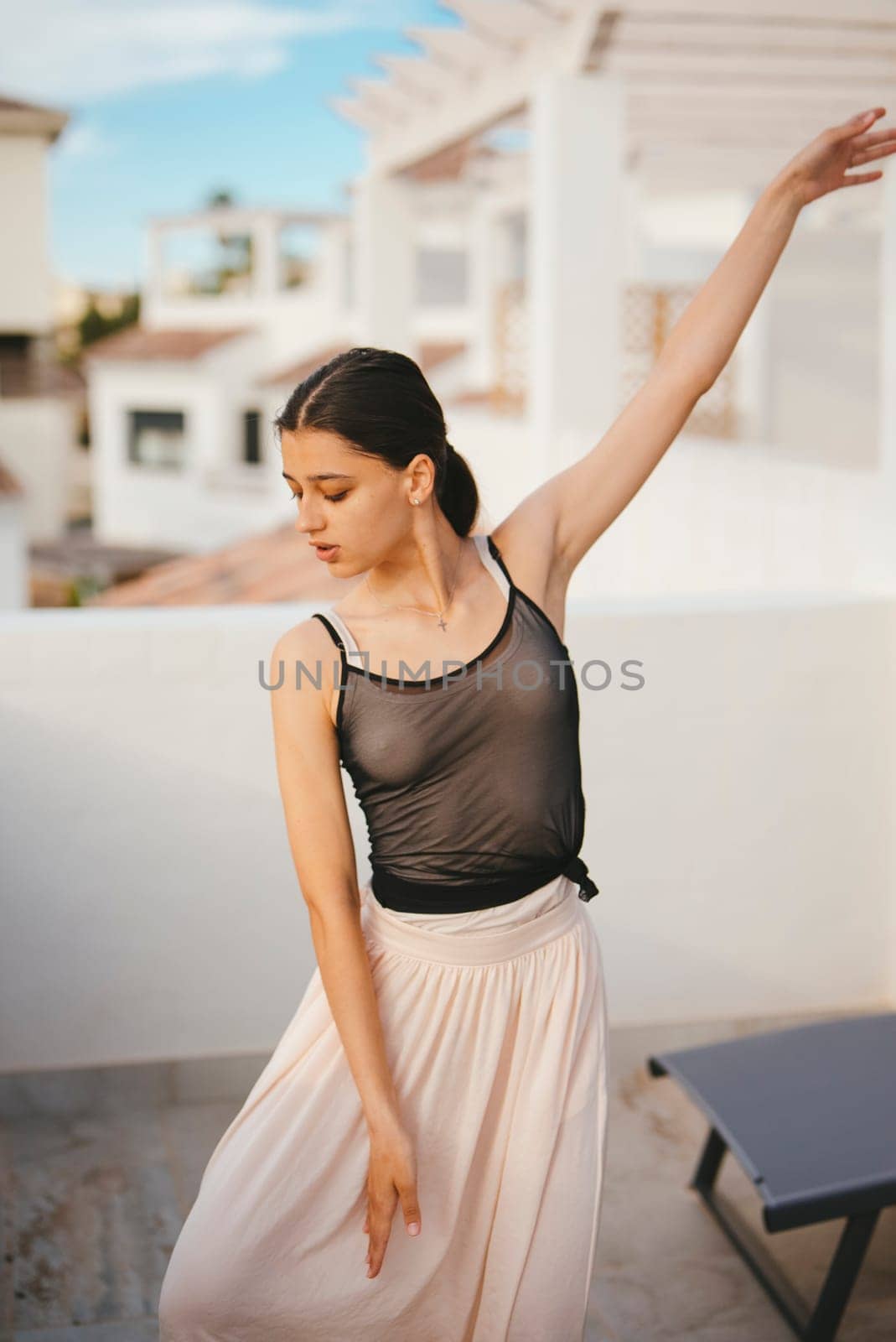 An elegant dancer strikes a wonderfully graceful pose while wearing a flowing outfit atop a sunlit rooftop