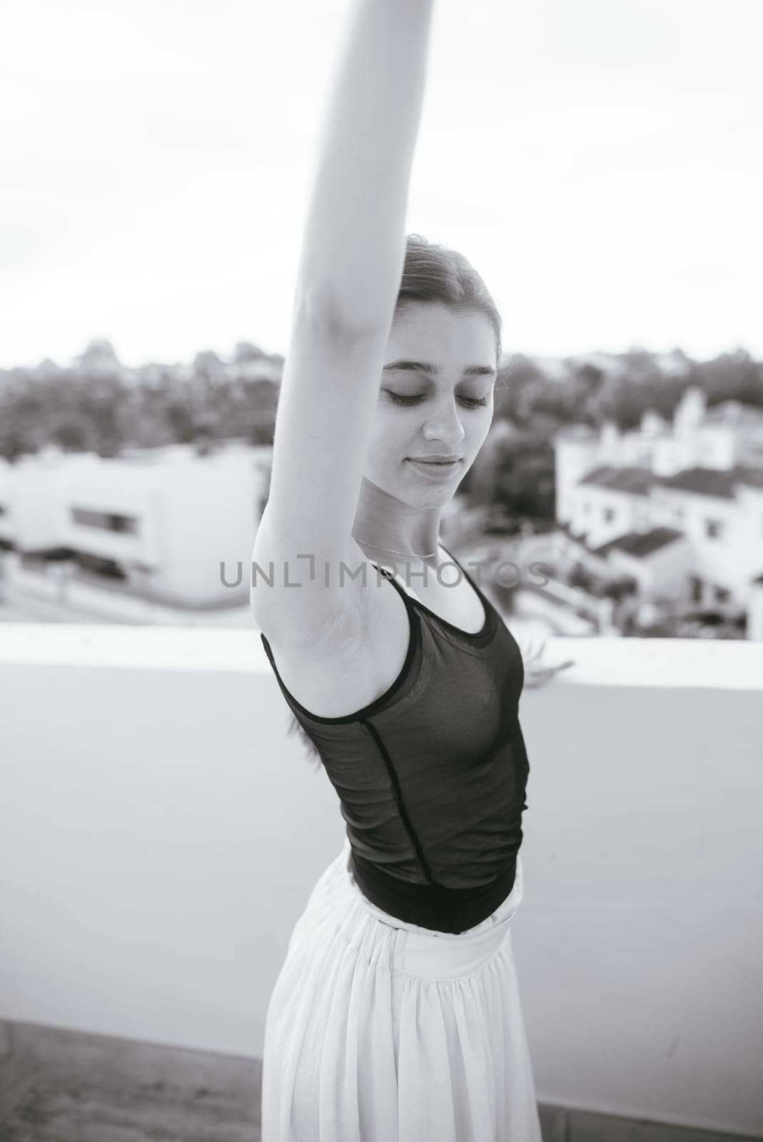 A graceful ballet dancer delicately raises her arm, beautifully showcased against an enchanting outdoor backdrop