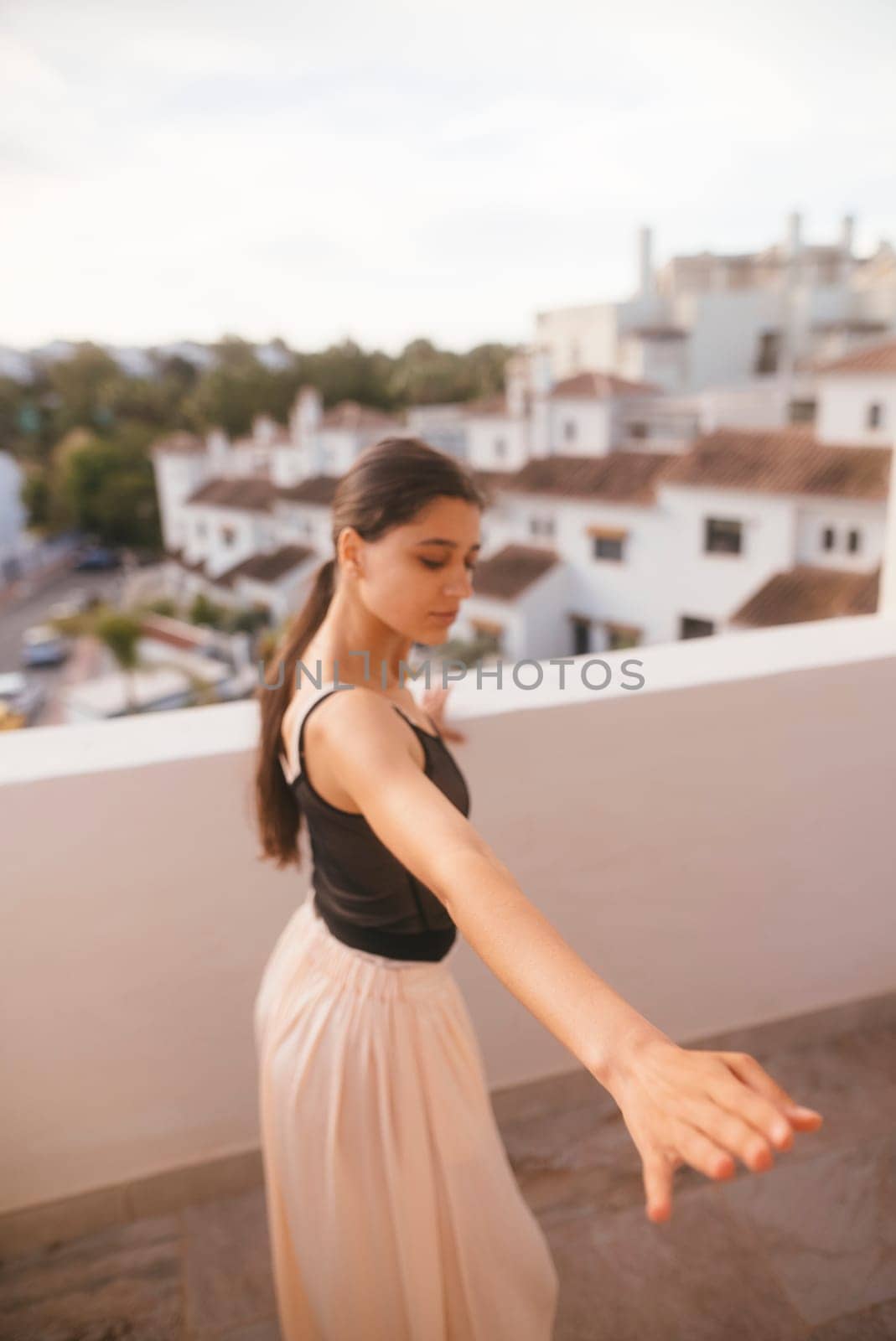 A graceful dancer elegantly strikes a dynamic pose on a sunlit balcony that offers stunning, breathtaking views