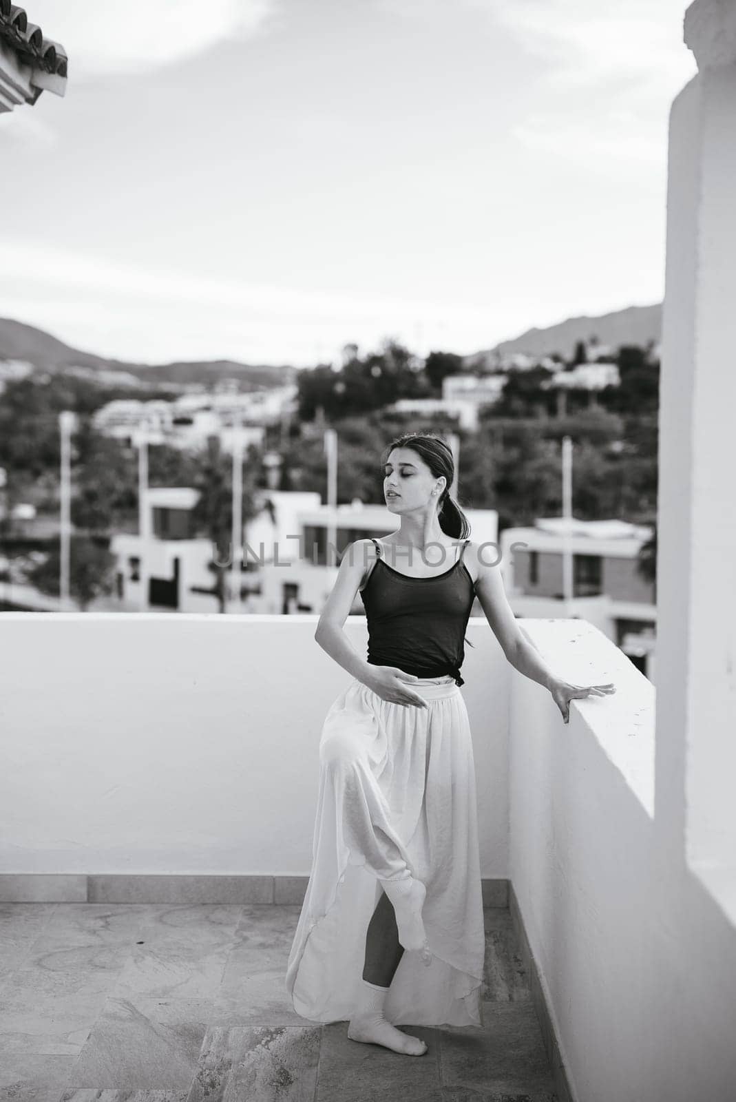 A young woman poses gracefully on a balcony, capturing a serene moment in black and white photography