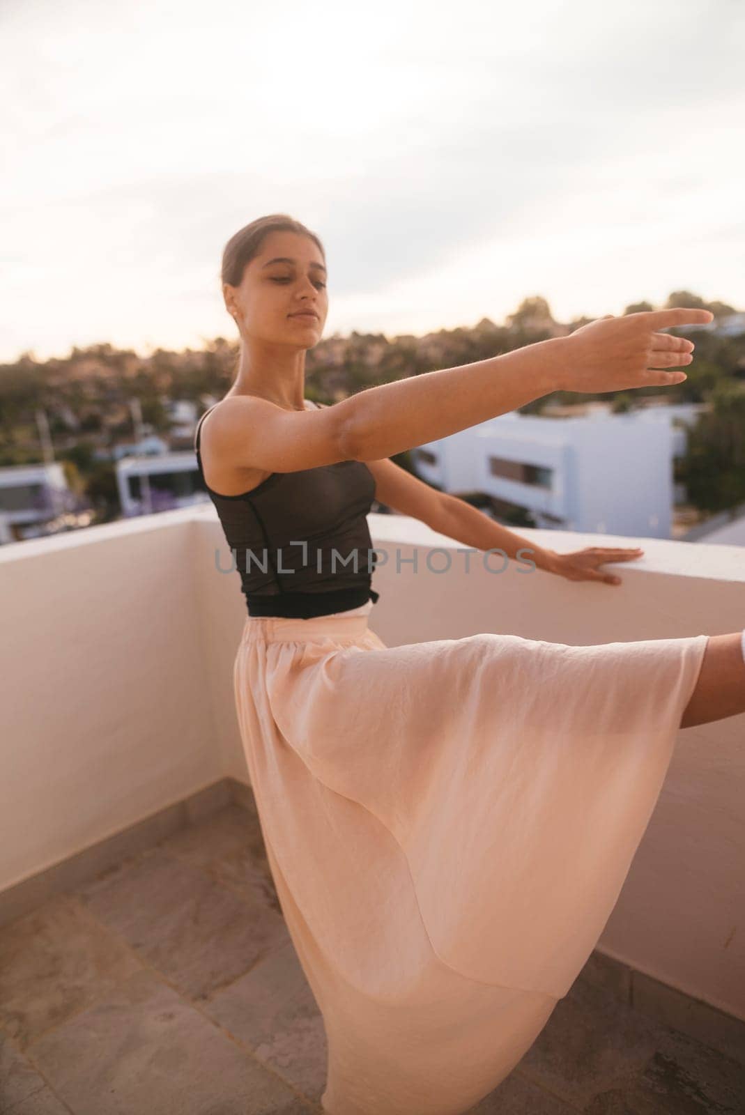 A dancer strikes a dramatic pose on a balcony at sunset, showcasing elegance and captivating beauty