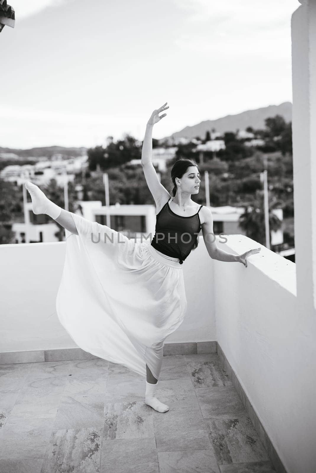 A breathtaking ballerina elegantly displays her poise and grace on a picturesque balcony with a scenic background