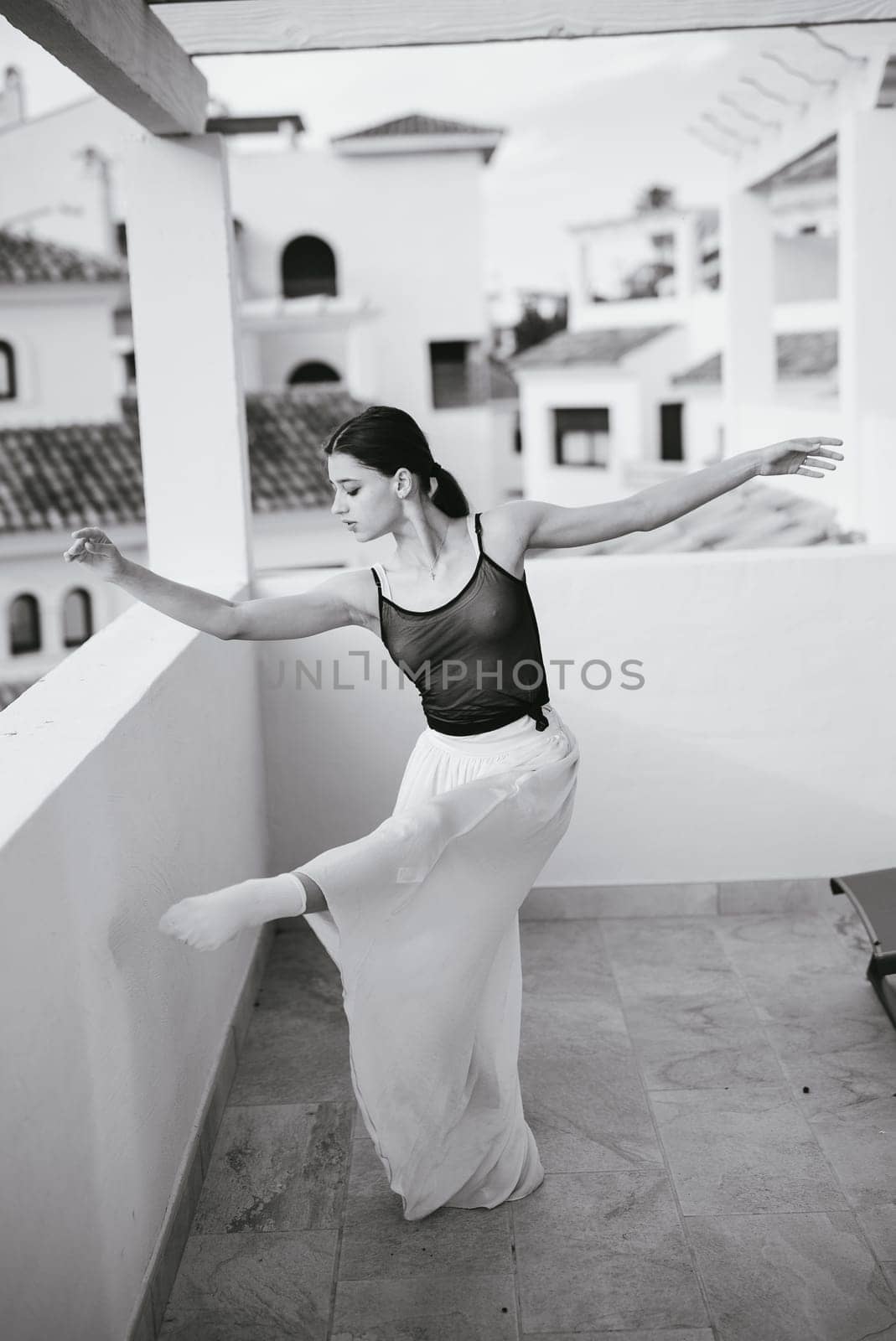 A dancer elegantly poses on a balcony, showcasing movement and artistry in a stunning black and white setting.