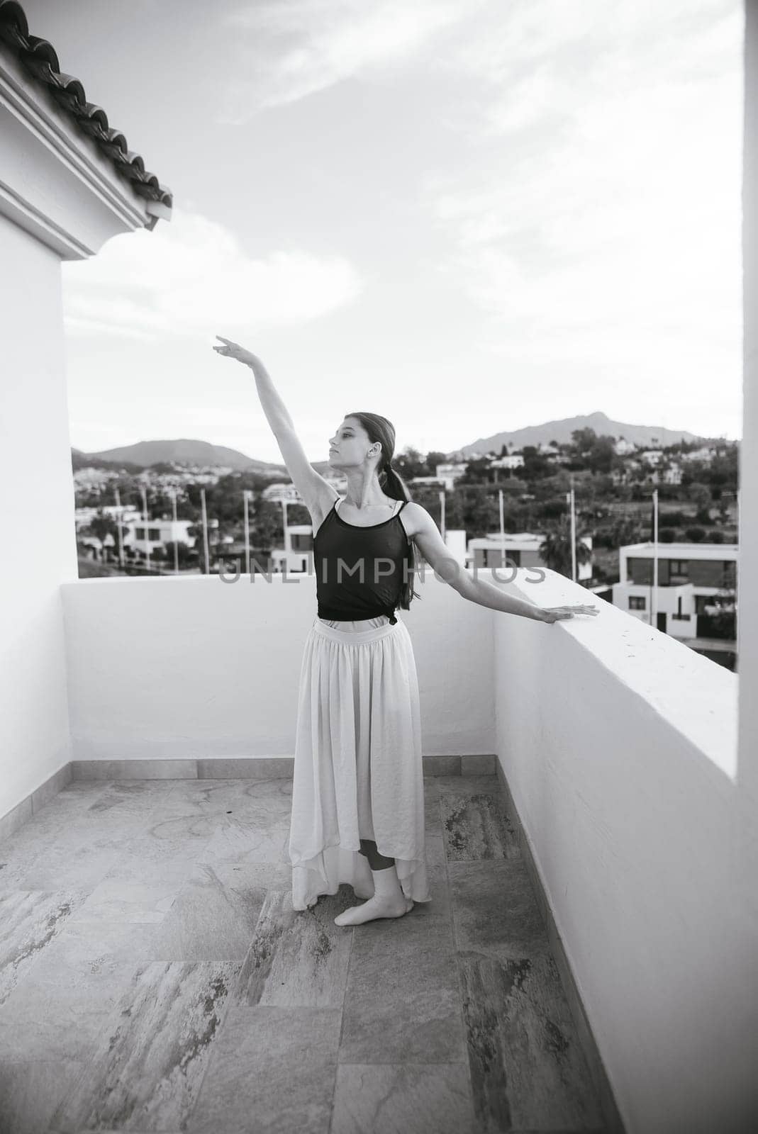 A talented dancer in elegantly flowy attire strikes a beautifully poised pose on a scenic, picturesque balcony