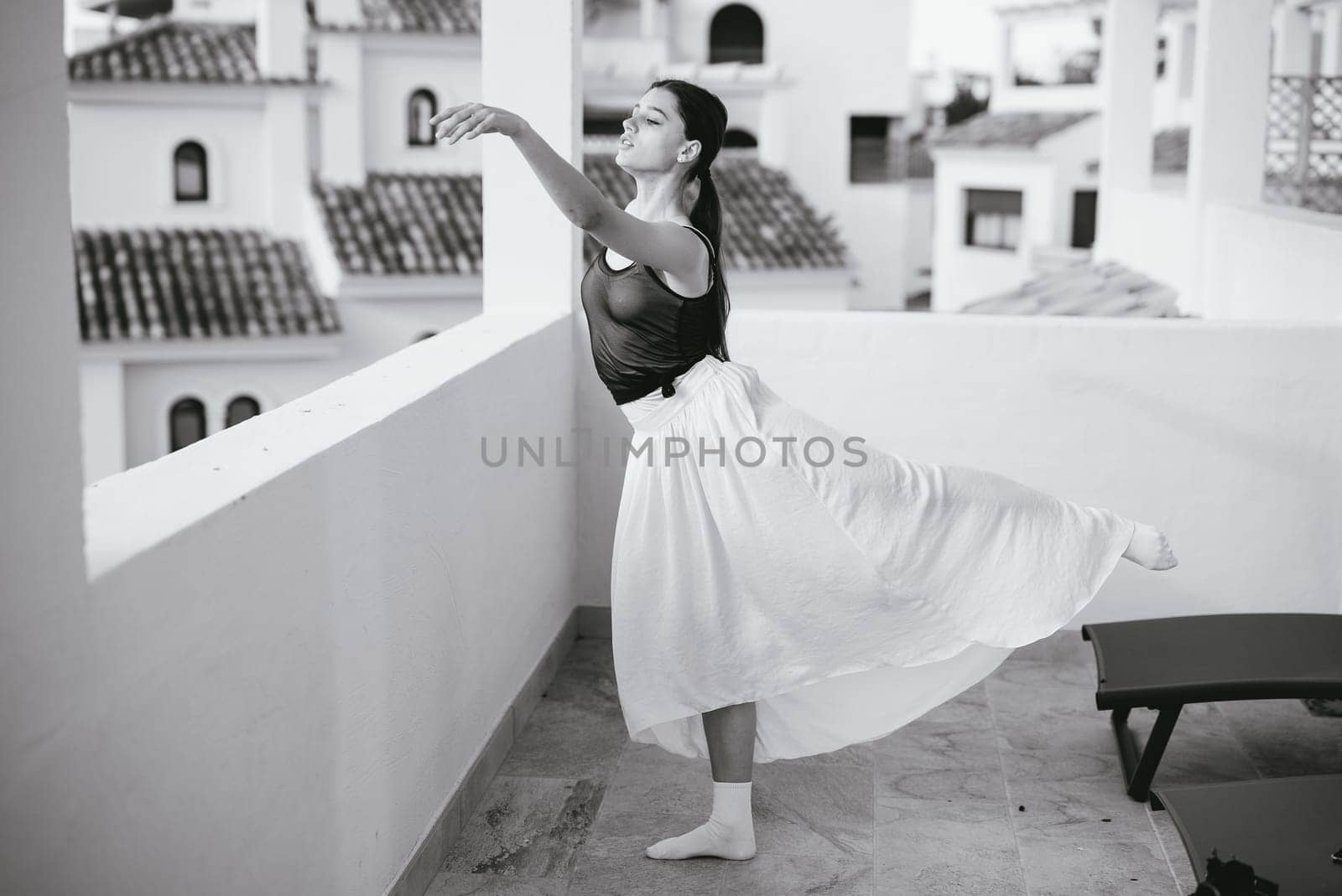 A graceful ballerina showcases her artistry on a sunlit balcony, captured in timeless black and white.