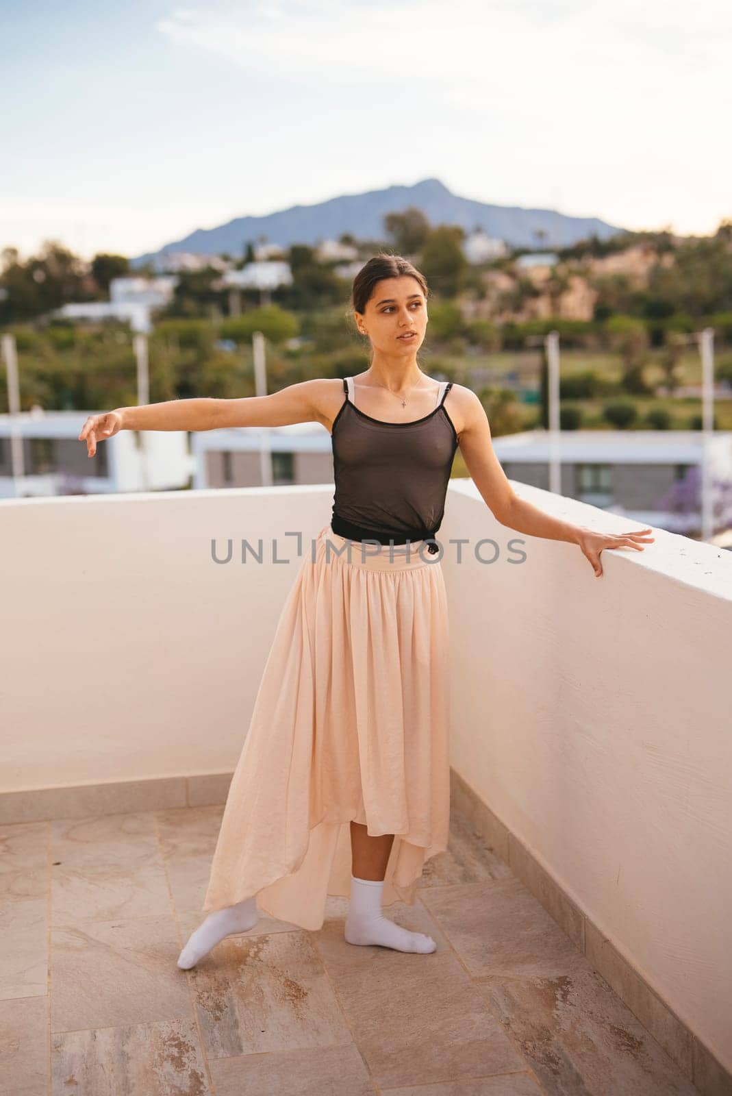 A graceful ballerina performs a stunning pose on a sunlit terrace with majestic mountains in the background