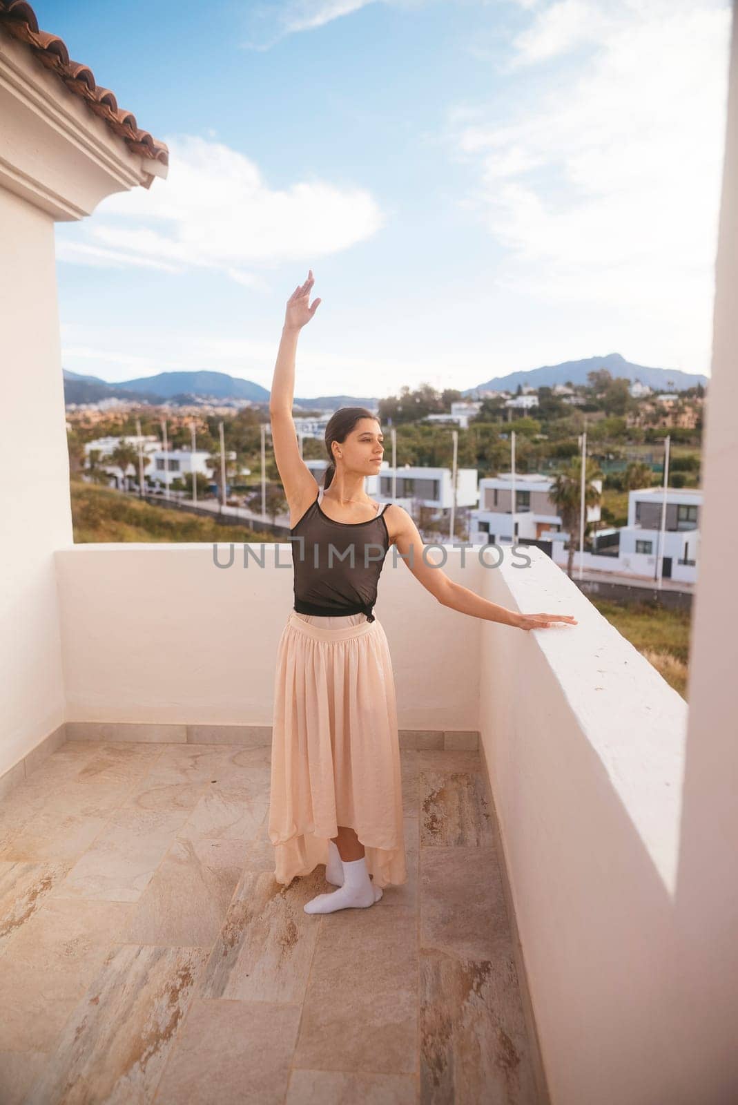 A talented dancer strikes a beautifully graceful pose on a balcony that features a stunning landscape backdrop