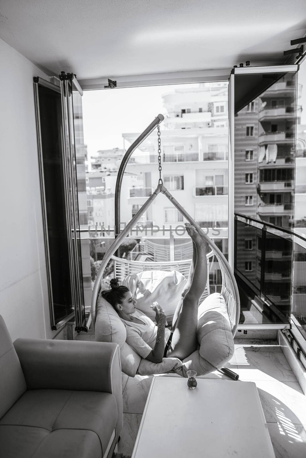 A lovely and cozy balcony scene features a person peacefully lounging in a stylish hanging chair, savoring the warm sun