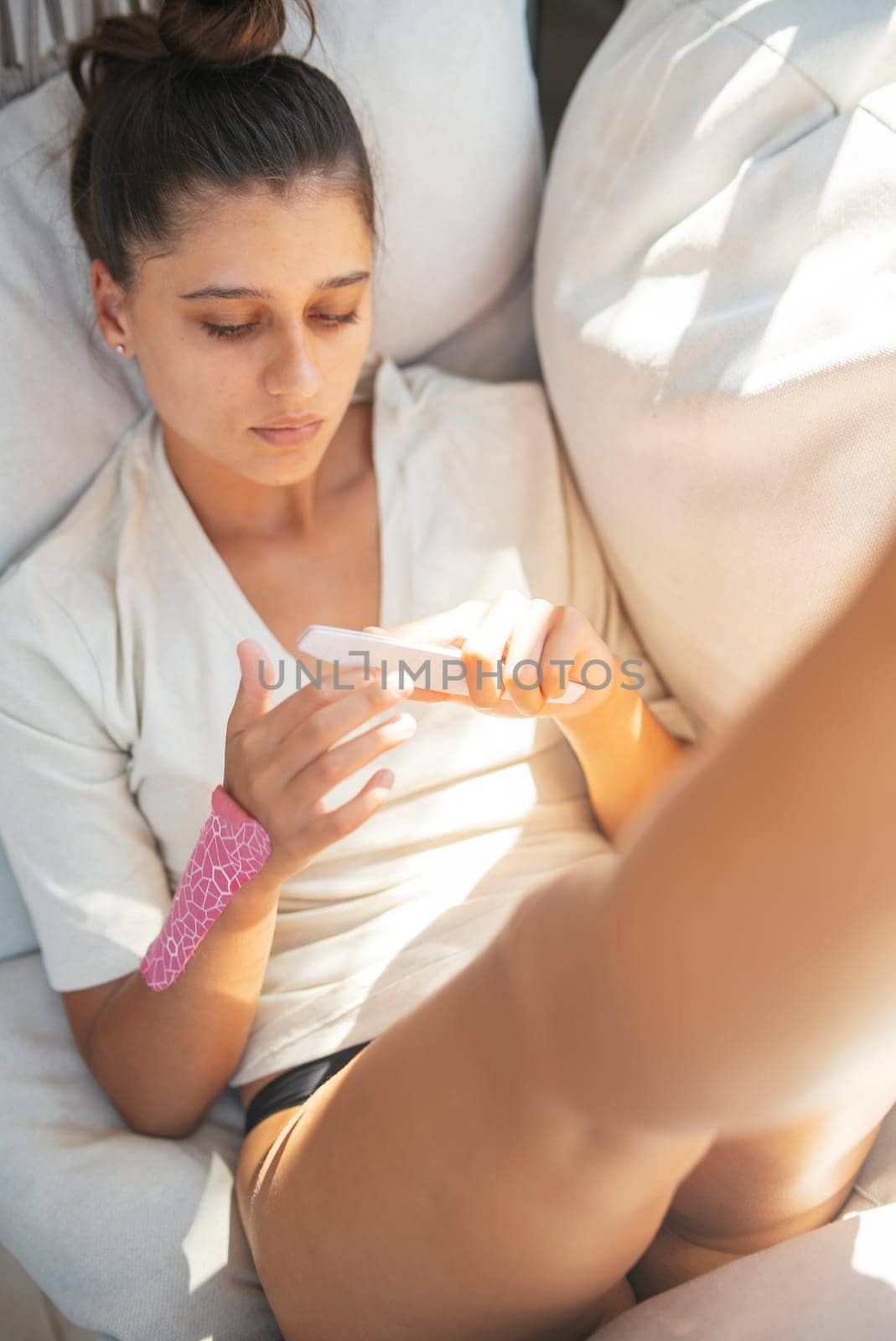 A young woman is lounging comfortably on a couch, deeply engaged with her smartphone in a cozy and relaxed setting